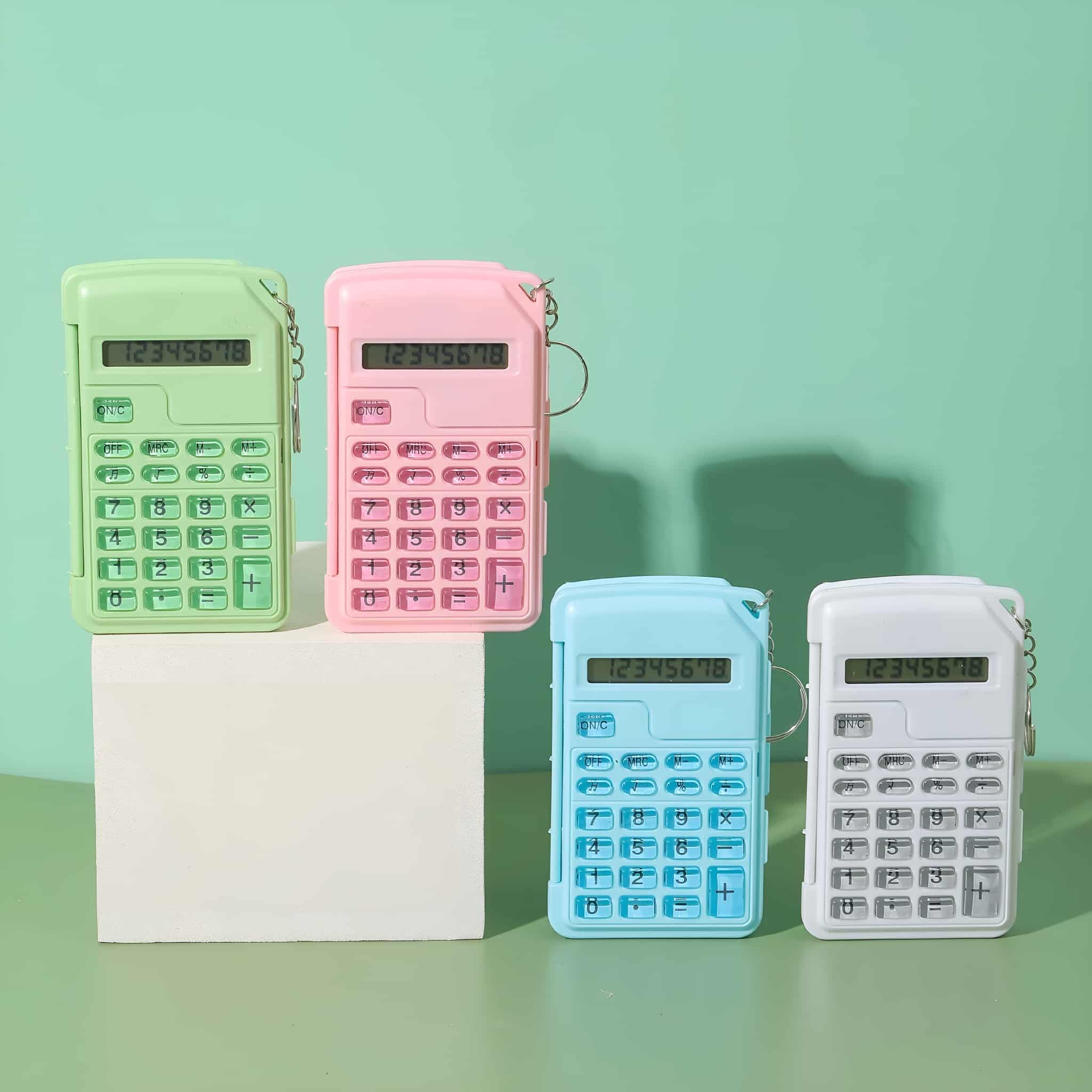 Vier farbige Taschenrechner sind auf einem weißen Block und einem grünen Hintergrund angeordnet.