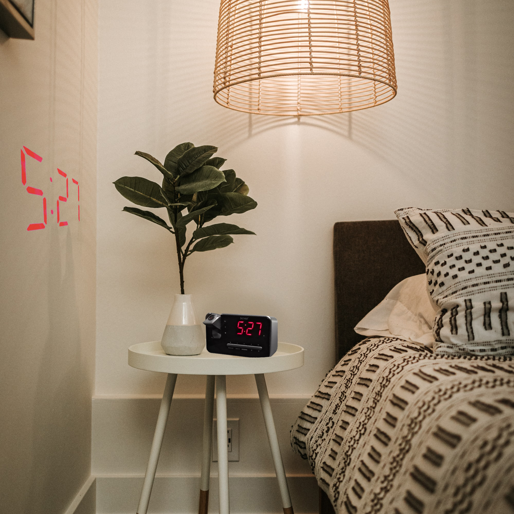 Bedroom scene: Alarm clock on table, plant, and time 5:27 projected on wall, with bed in background.