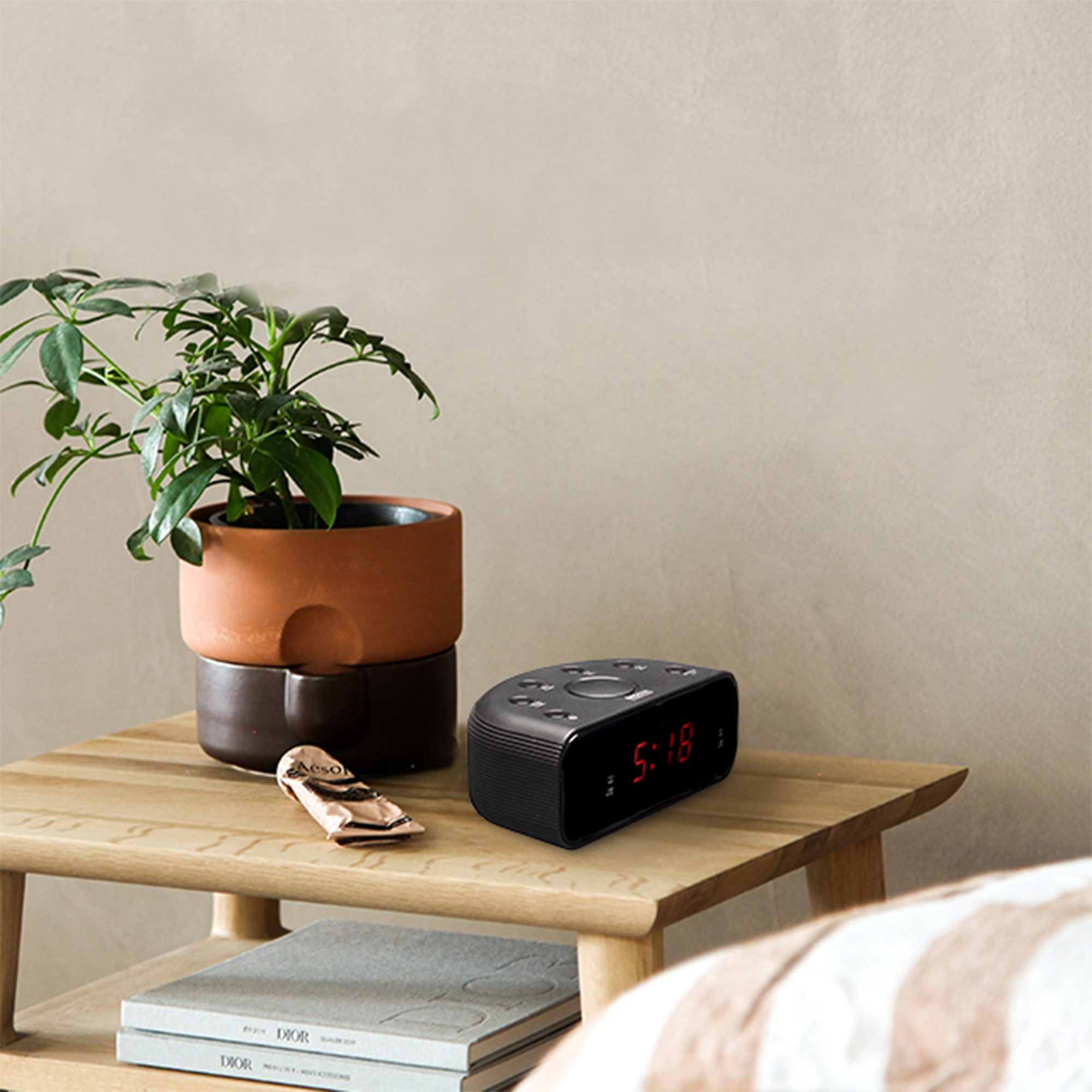 Czarny budzik na drewnianym stoliku obok rośliny.