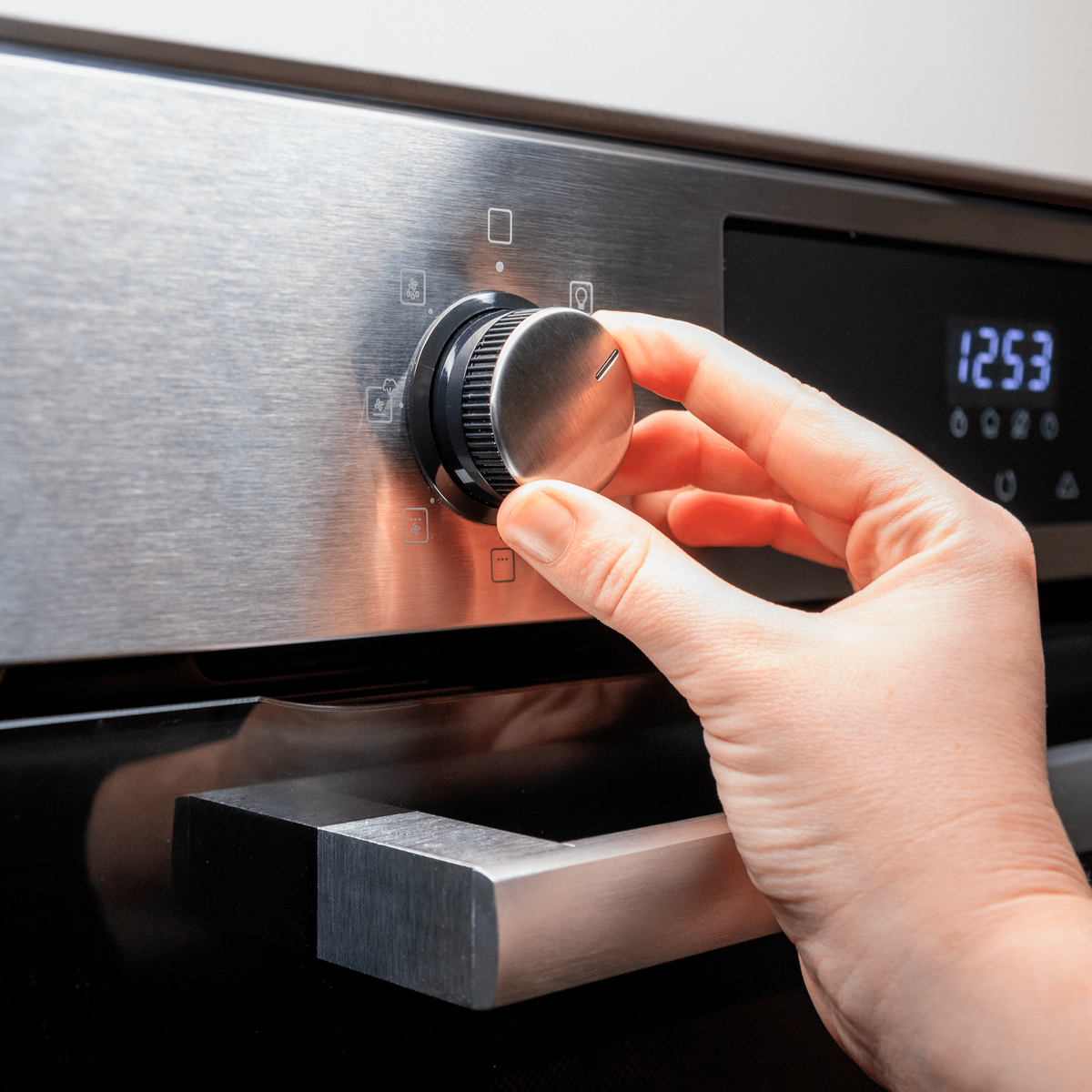 Mano che gira la manopola nera del forno, forno in acciaio inox.