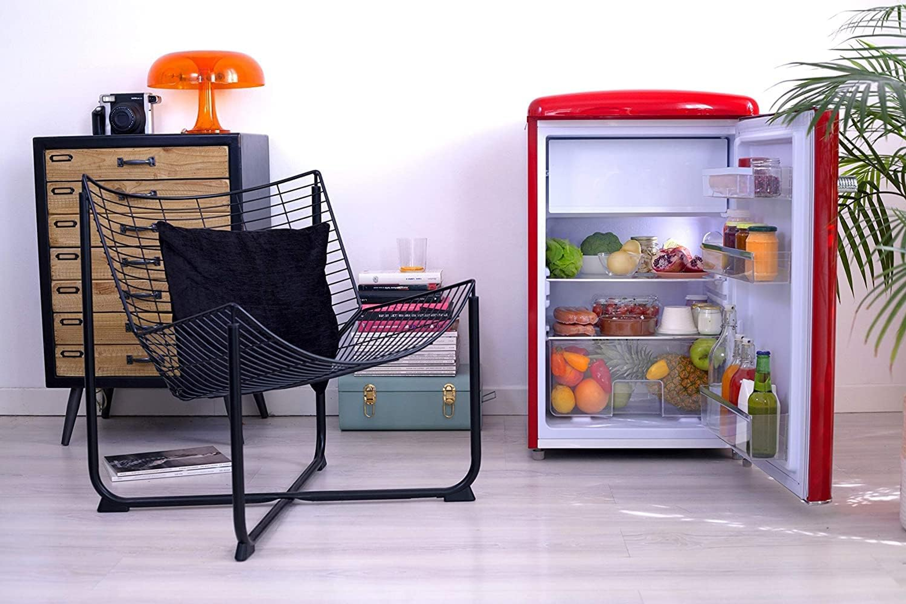 Roter Retro-Kühlschrank mit offener Tür, die Lebensmittel zeigt. Schwarzer Stuhl und orangefarbene Lampe im Hintergrund.