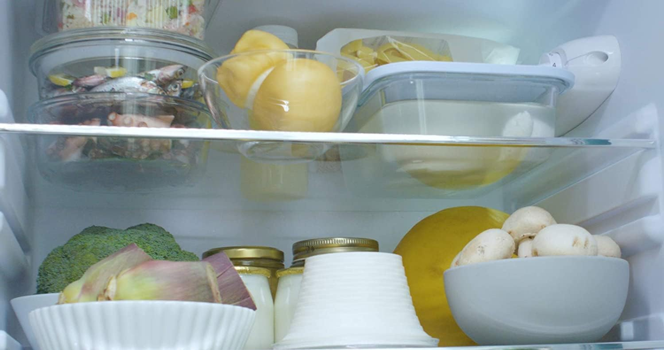 Kühlschrank-Innenraum mit Glasböden. Enthält Lebensmittel in Behältern und verschiedene Produkte.