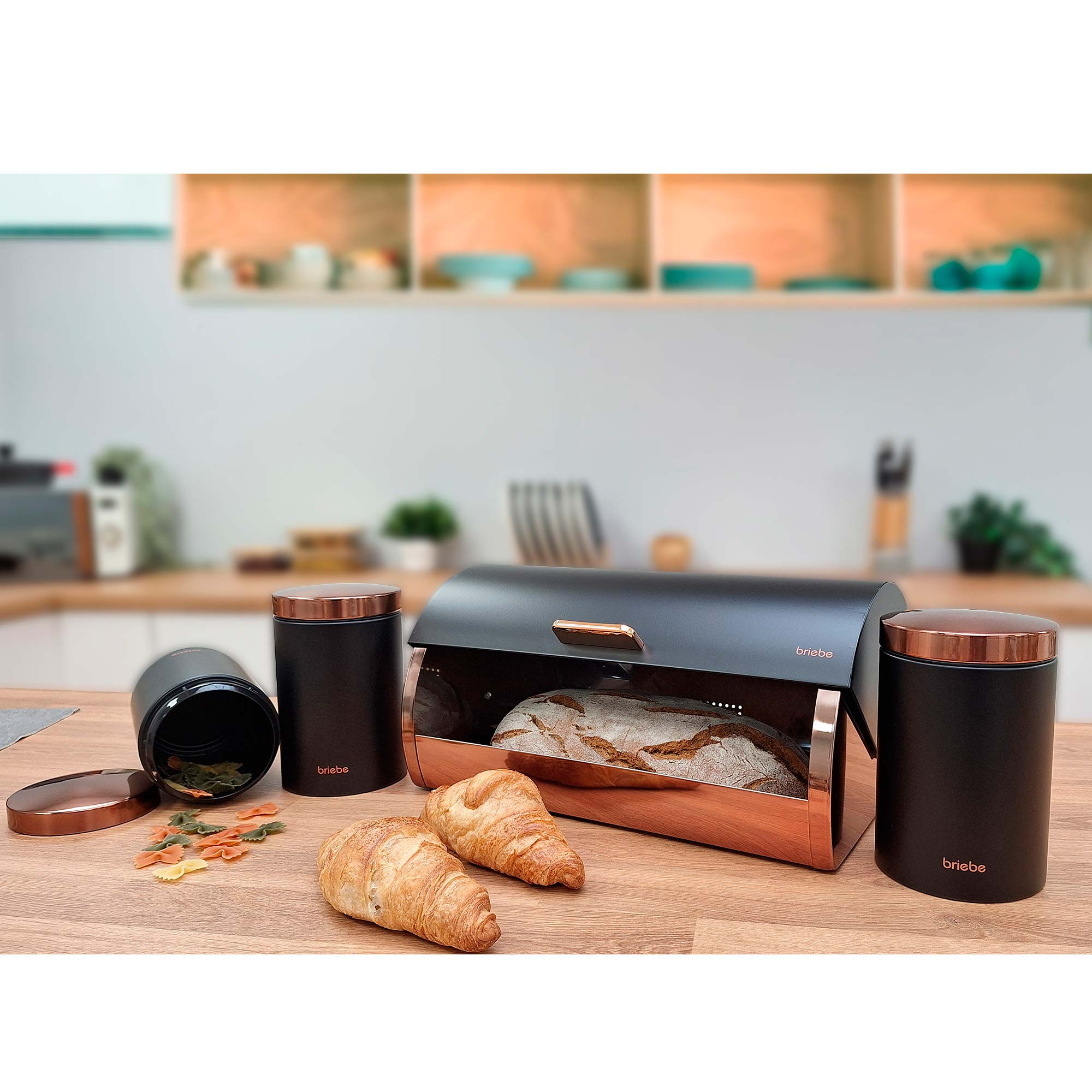 Brot und Croissants in einer Brotdose mit zwei Gläsern und Nudeln auf einem Holztisch.