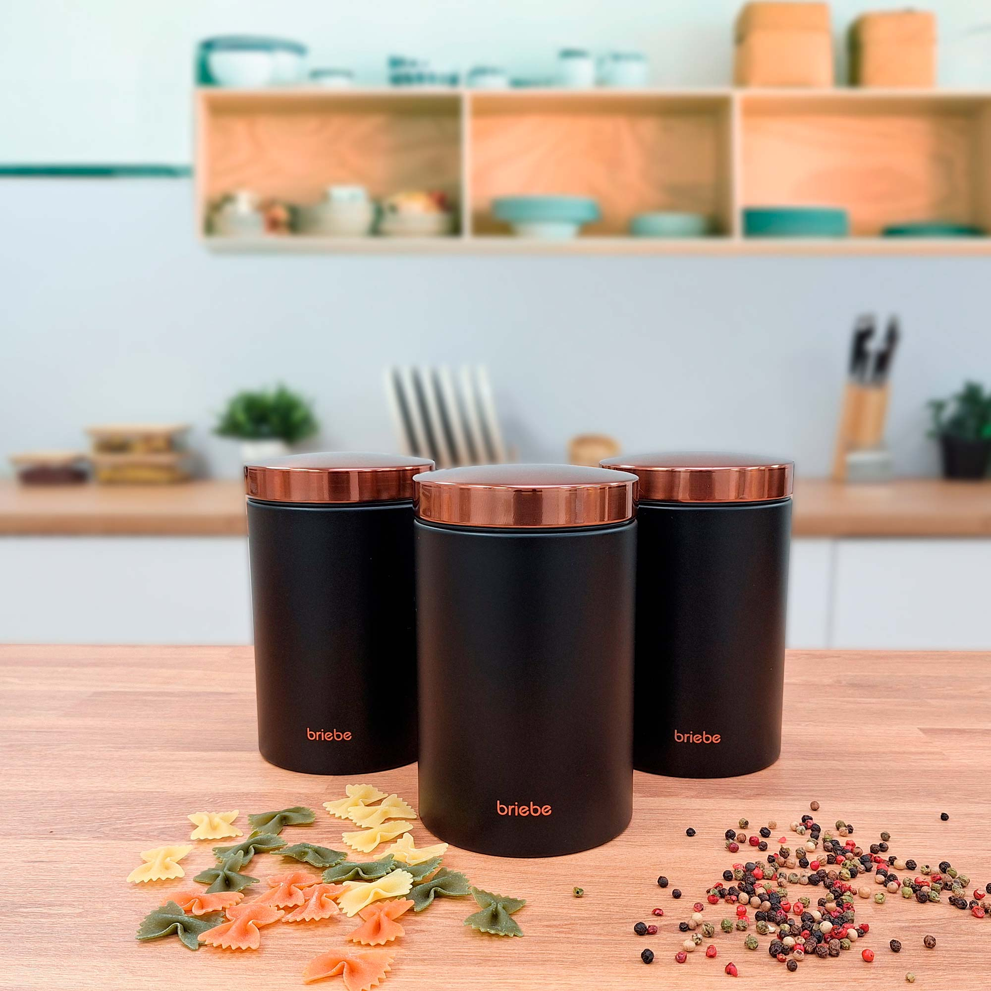 Drei schwarze Gläser mit Kupferdeckeln auf Holztisch, Nudeln und Gewürze.