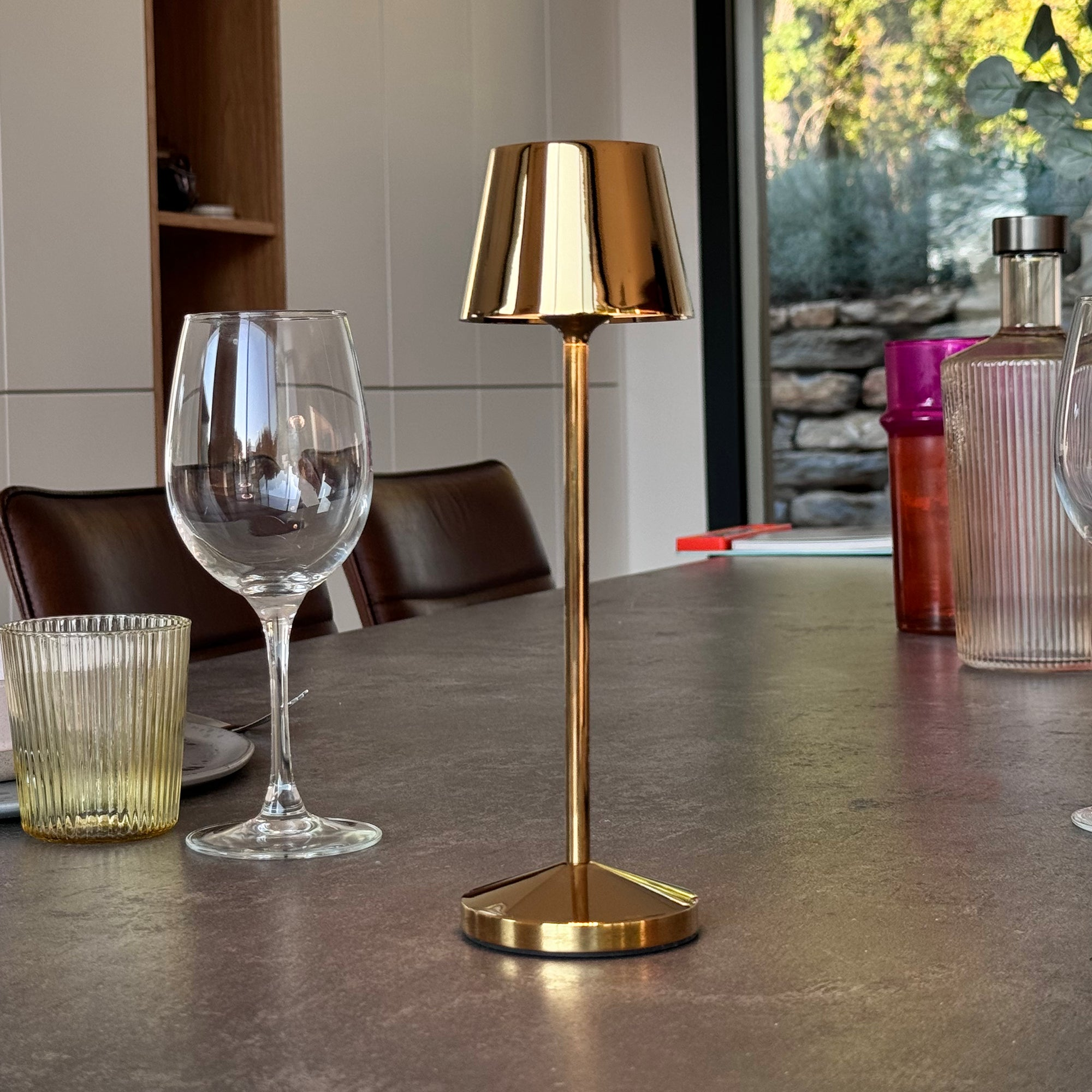 Eine goldene Tischlampe auf einem Tisch mit einem Weinglas und einem Wasserglas.