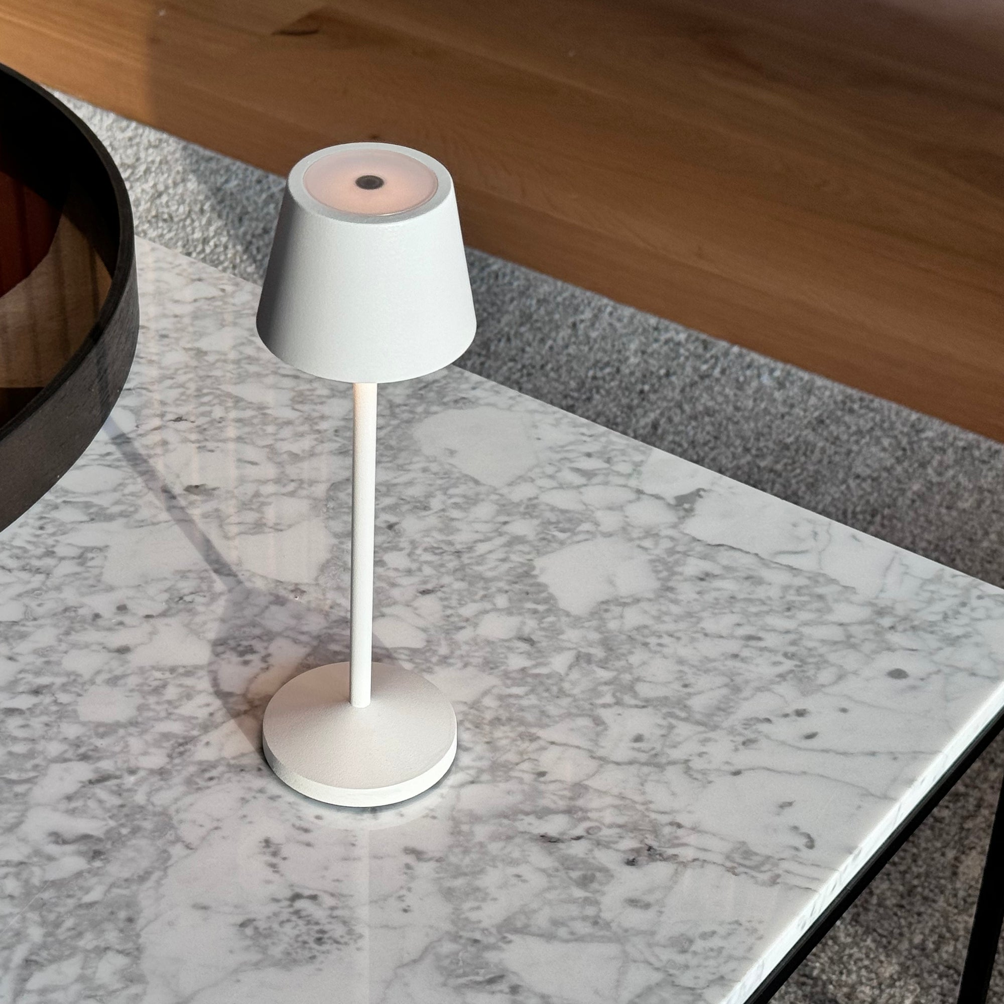 Eine weiße Tischlampe mit weißem Schirm und Fuß auf einem Marmortisch, auf einem Teppich.