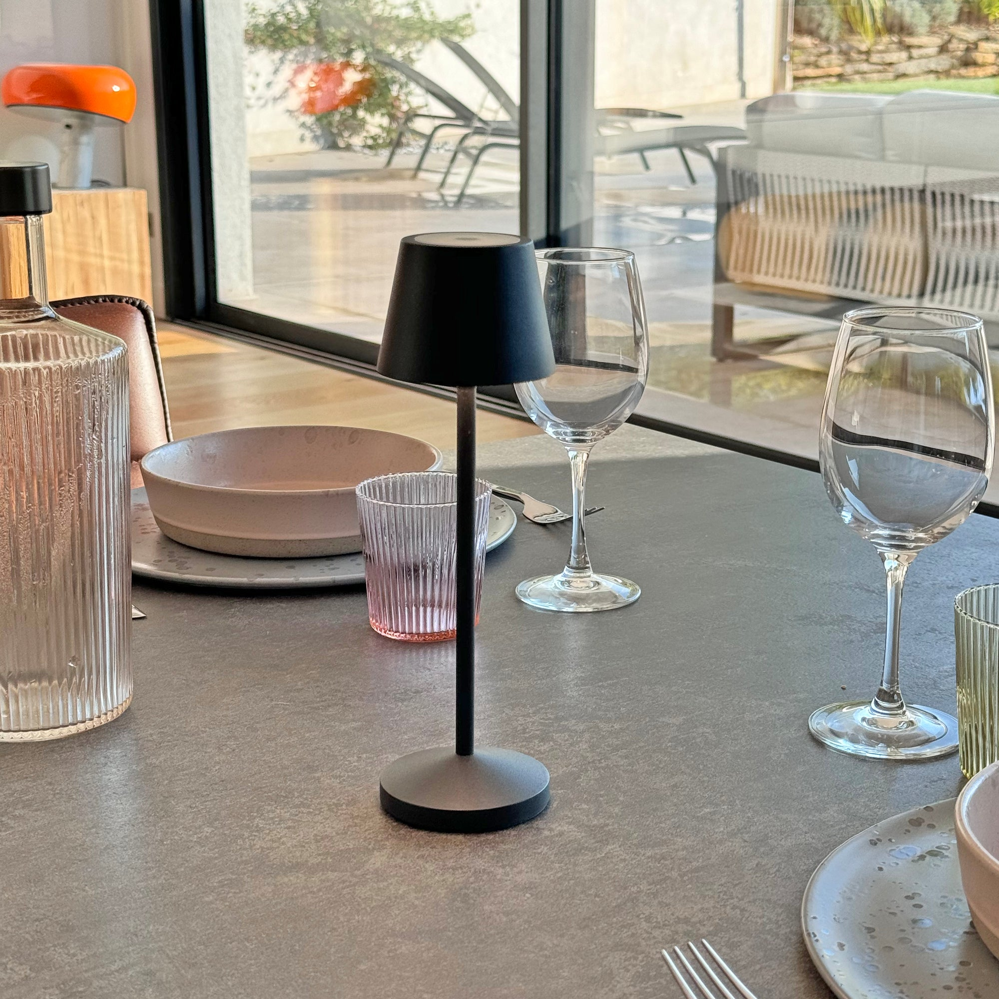 Tisch mit schwarzer Lampe, Gläsern und einer Schüssel. Die Gläser sind rechts. Ein Tisch mit Gegenständen darauf.