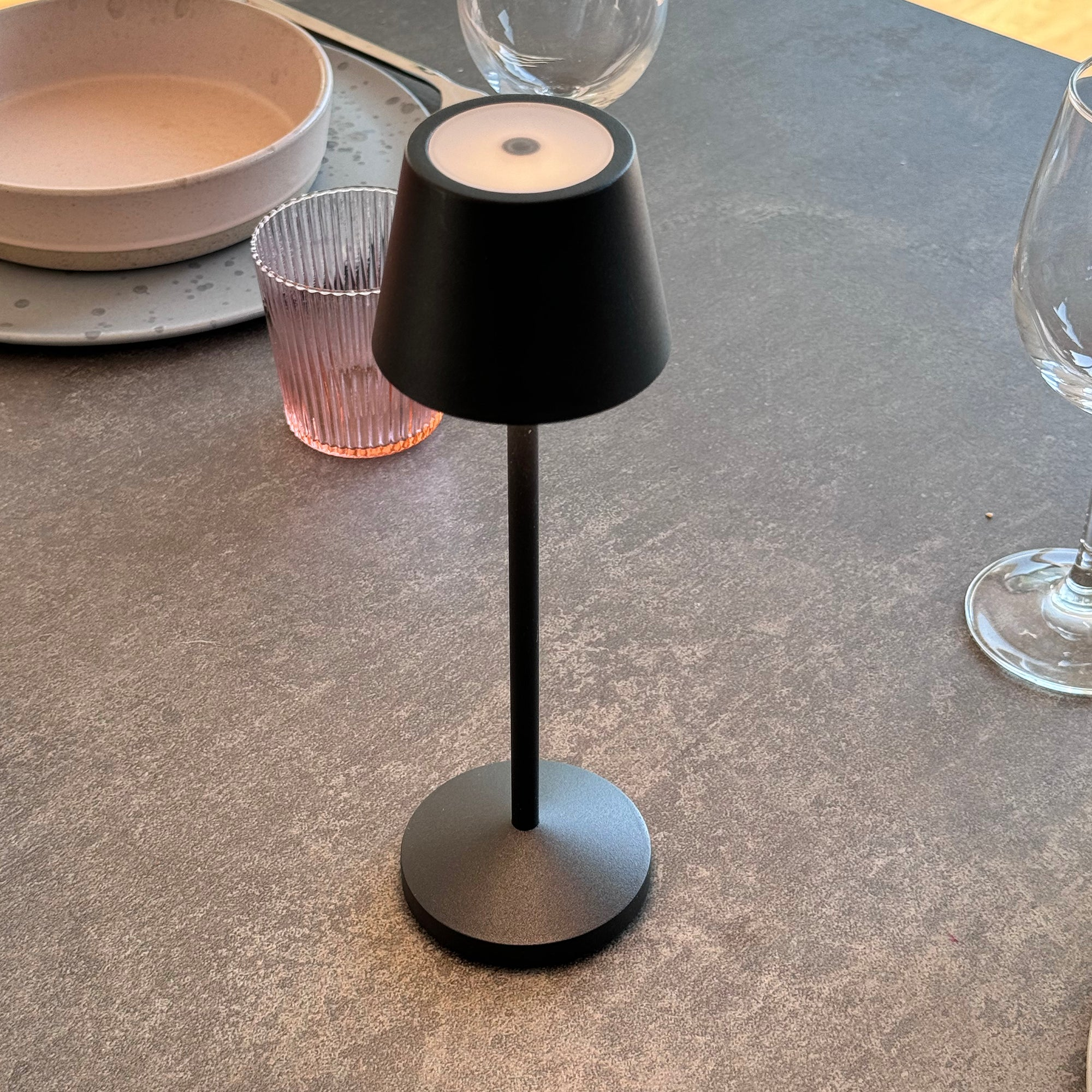 Schwarze Tischlampe auf einem Tisch, mit Glas und Teller in der Nähe.