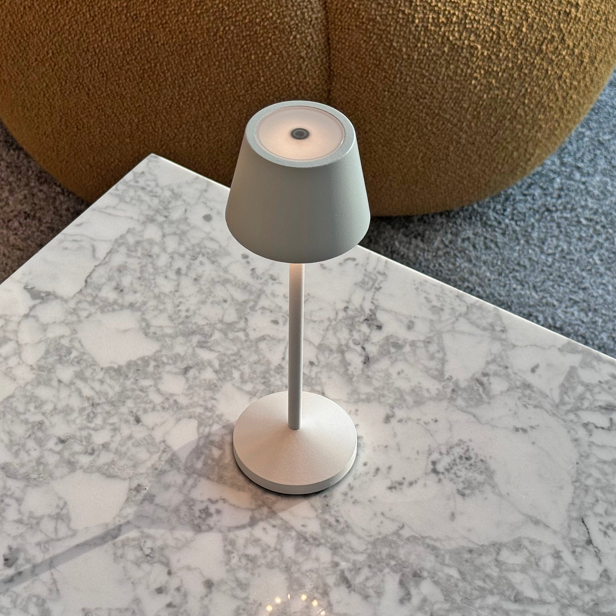 Eine kleine Tischlampe mit grauem Schirm auf einer Marmoroberfläche.