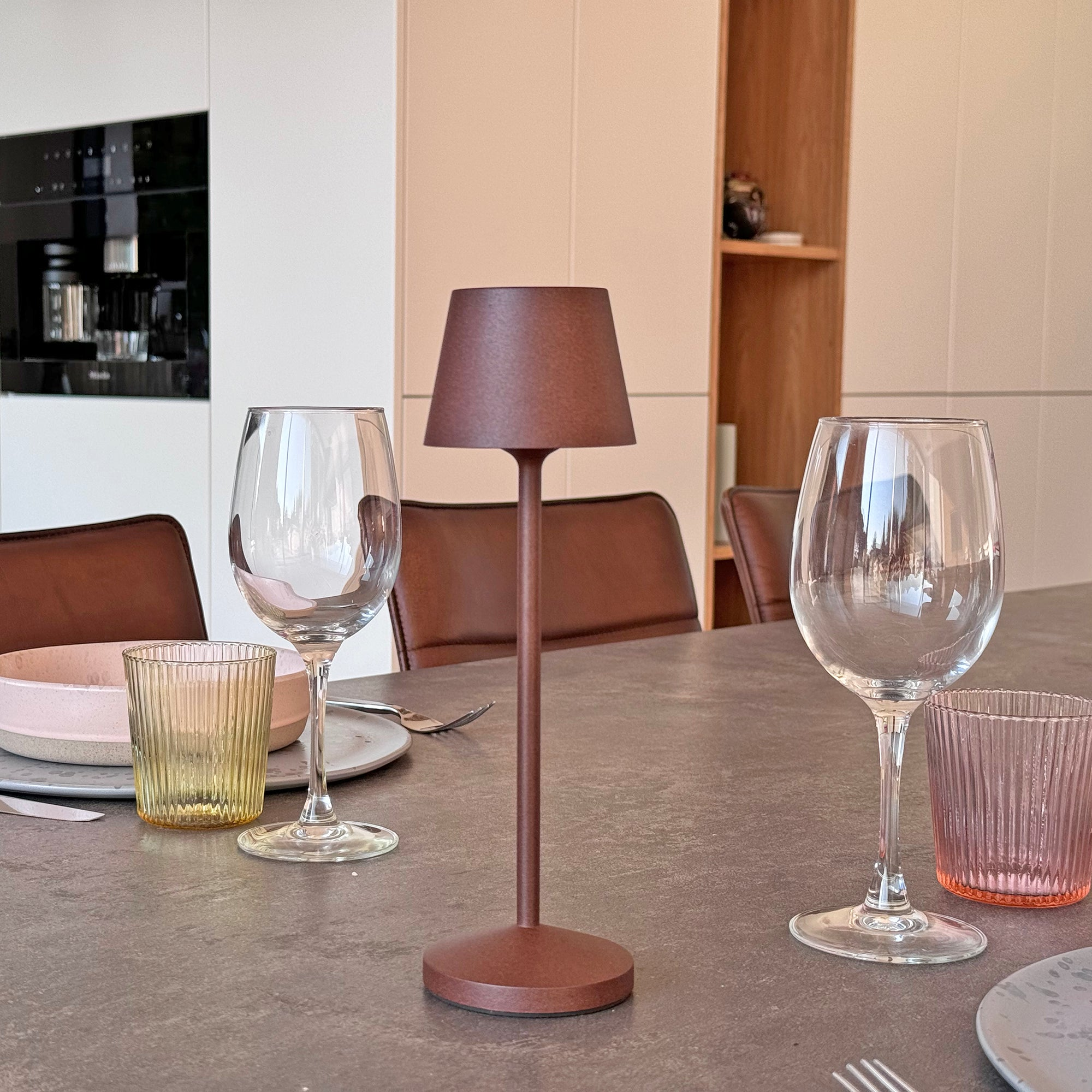 Braune Lampe auf einem Tisch. Zwei Weingläser und zwei weitere Gläser stehen darum herum.
