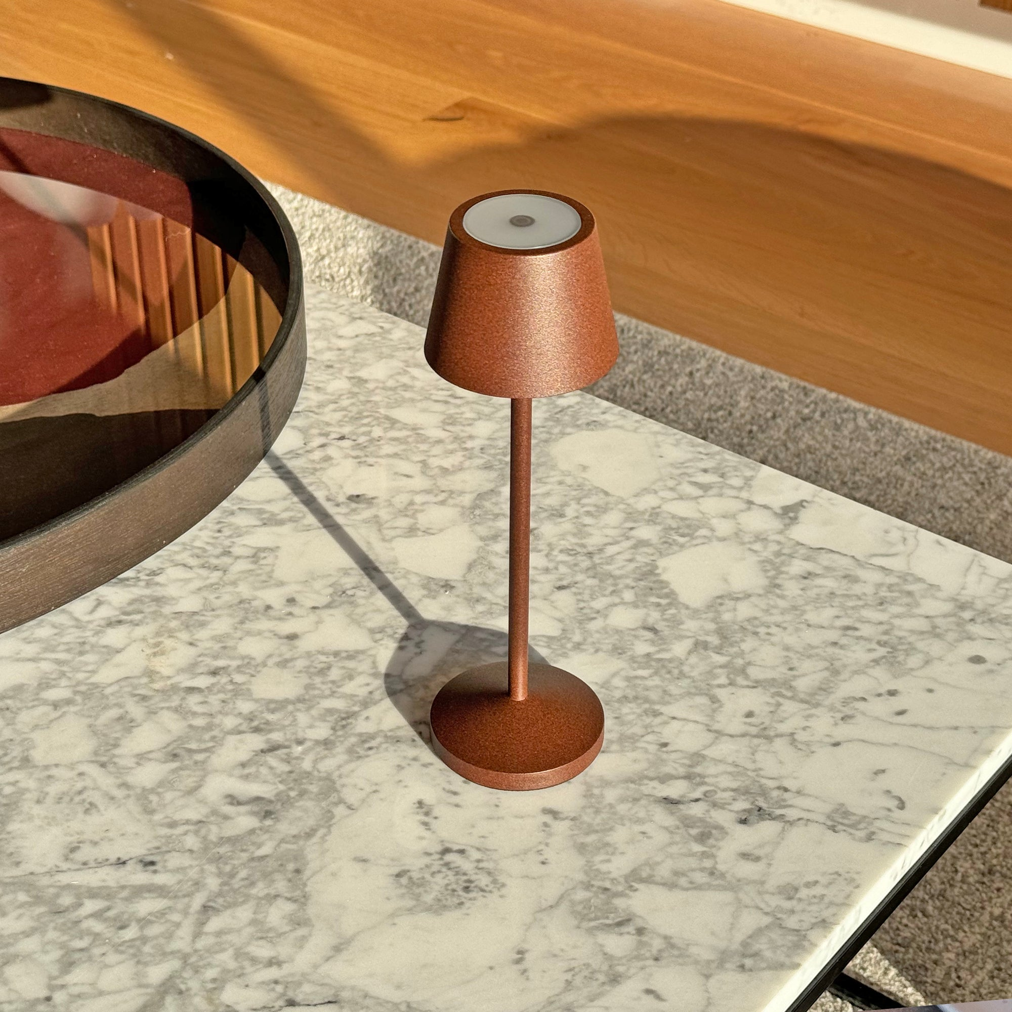 Braune Tischlampe auf einem Marmortisch. Die Lampe hat einen braunen Sockel und Schirm. Sonnenlicht und Schatten.