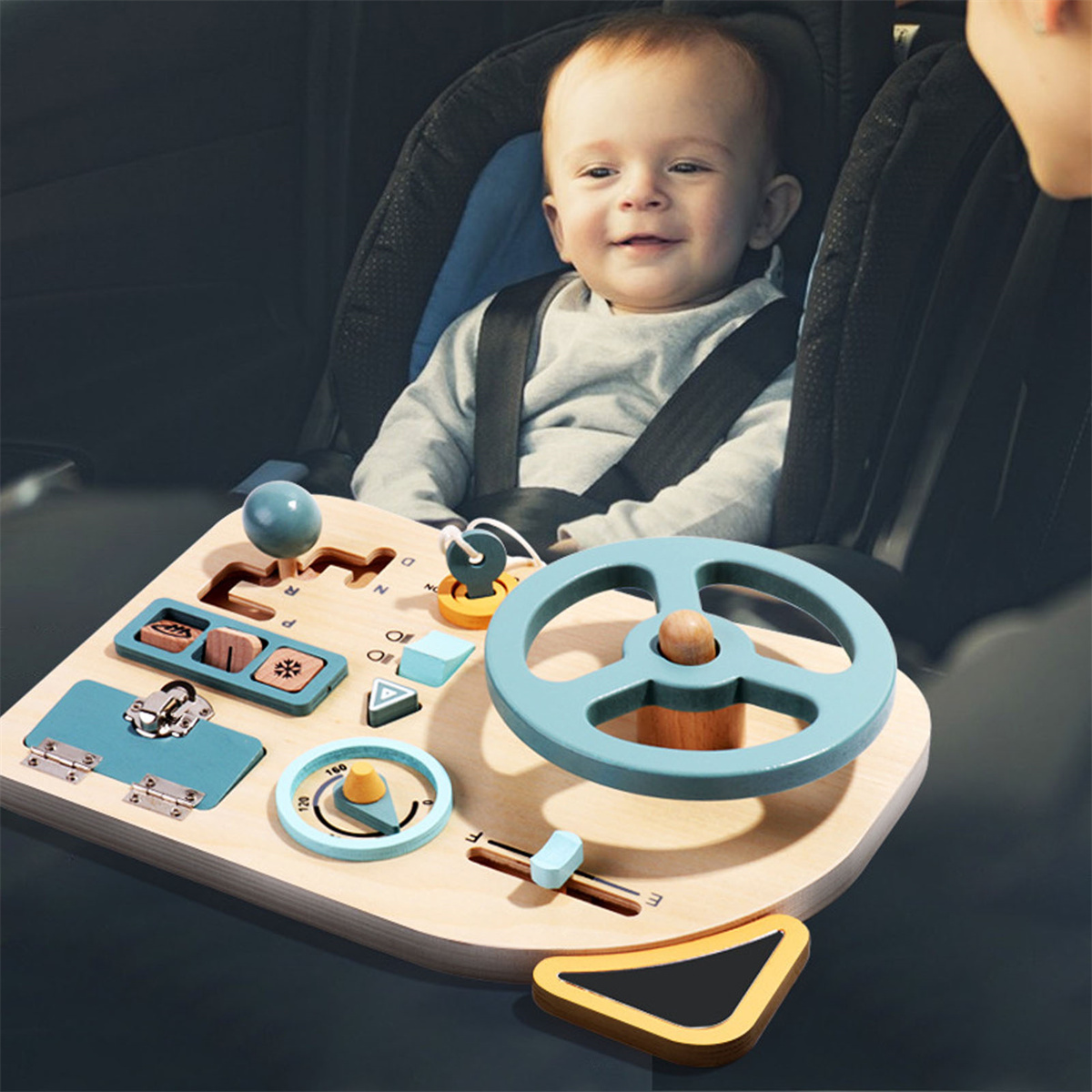 Baby in einem Autositz lächelt in die Kamera, während es mit einem hölzernen Autospielzeug spielt.