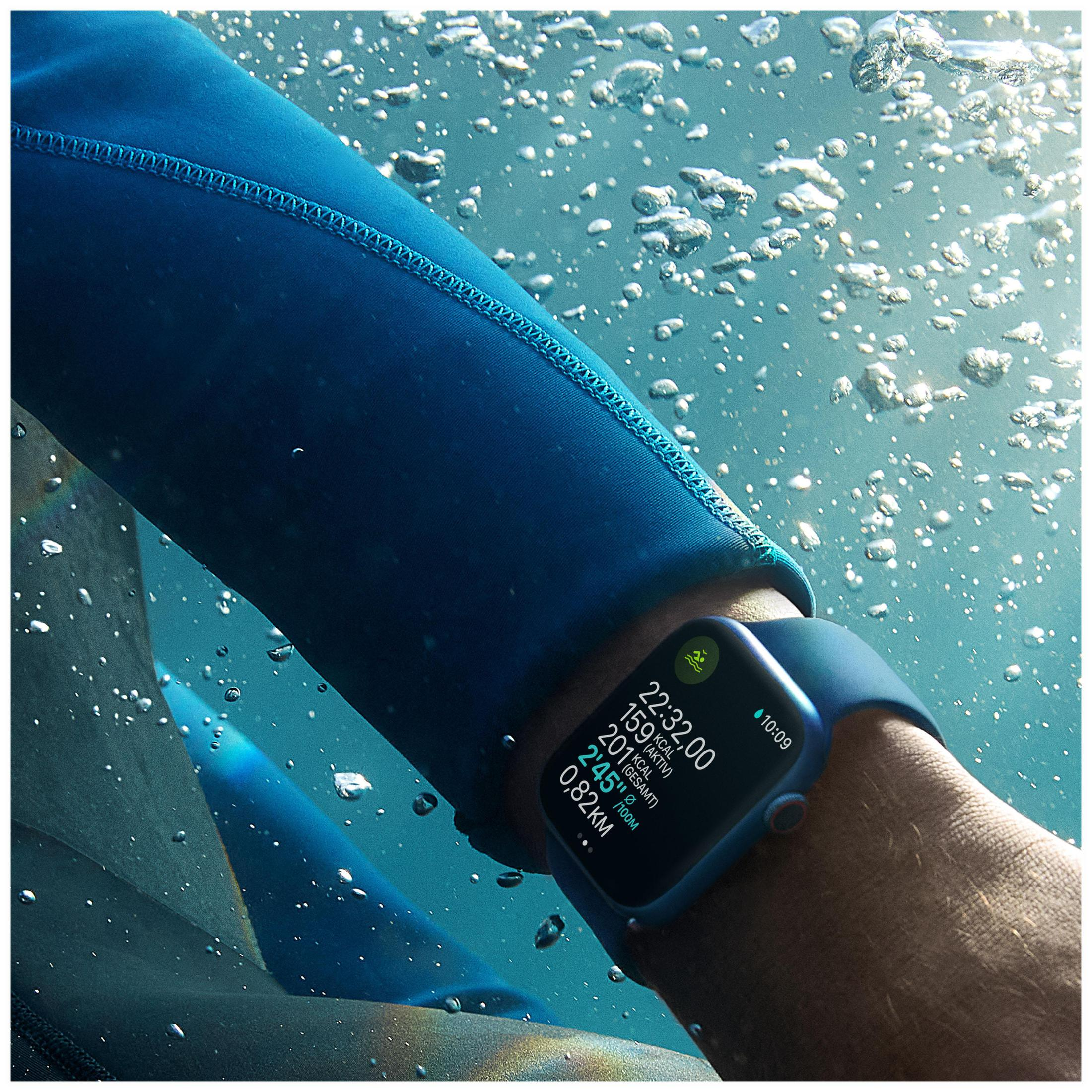 Un braccio di una persona con una muta blu e un Apple Watch blu sott'acqua, che mostra l'ora e i dati.