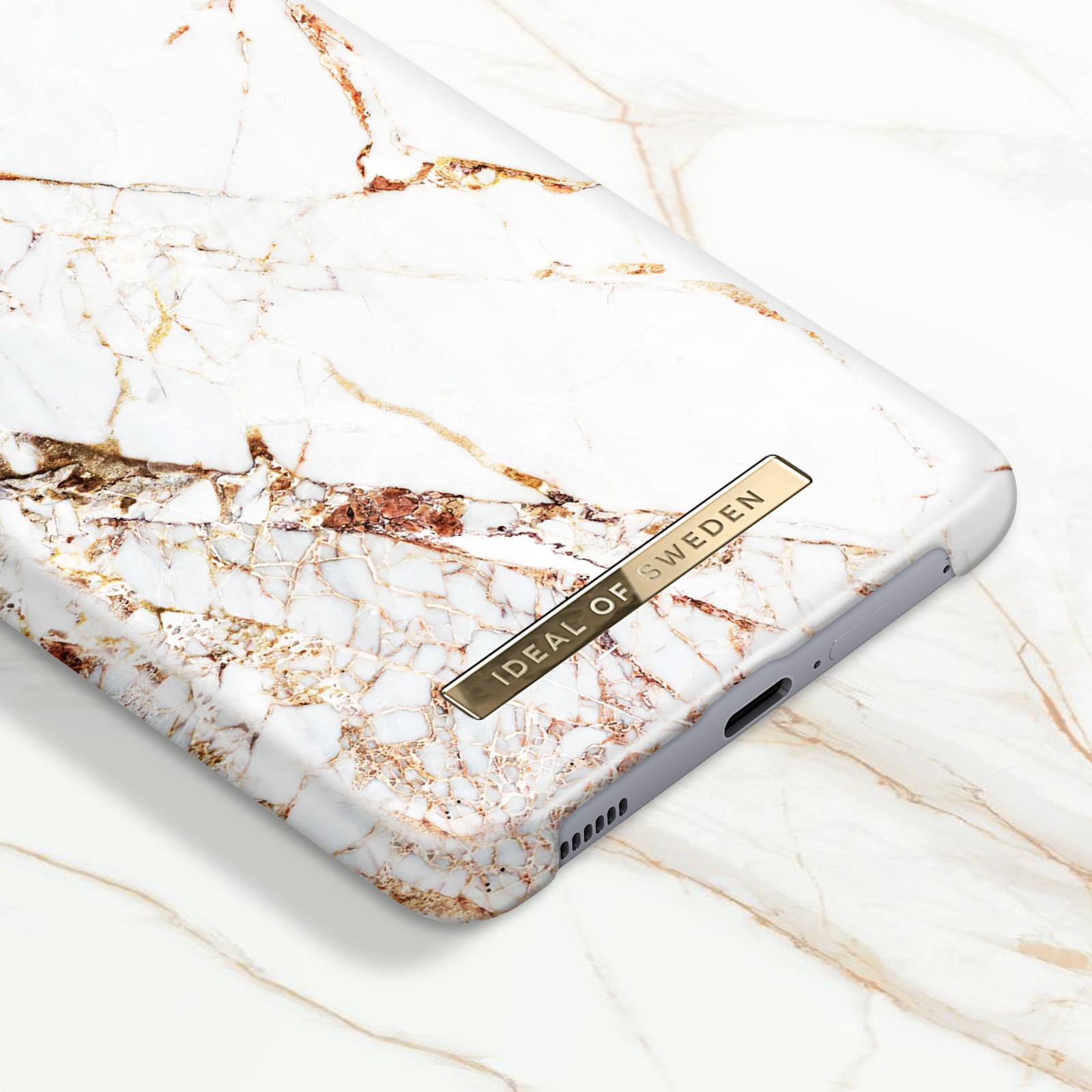 Custodia per telefono in marmo bianco e oro. Etichetta dorata Ideal of Sweden. Sfondo in marmo bianco.