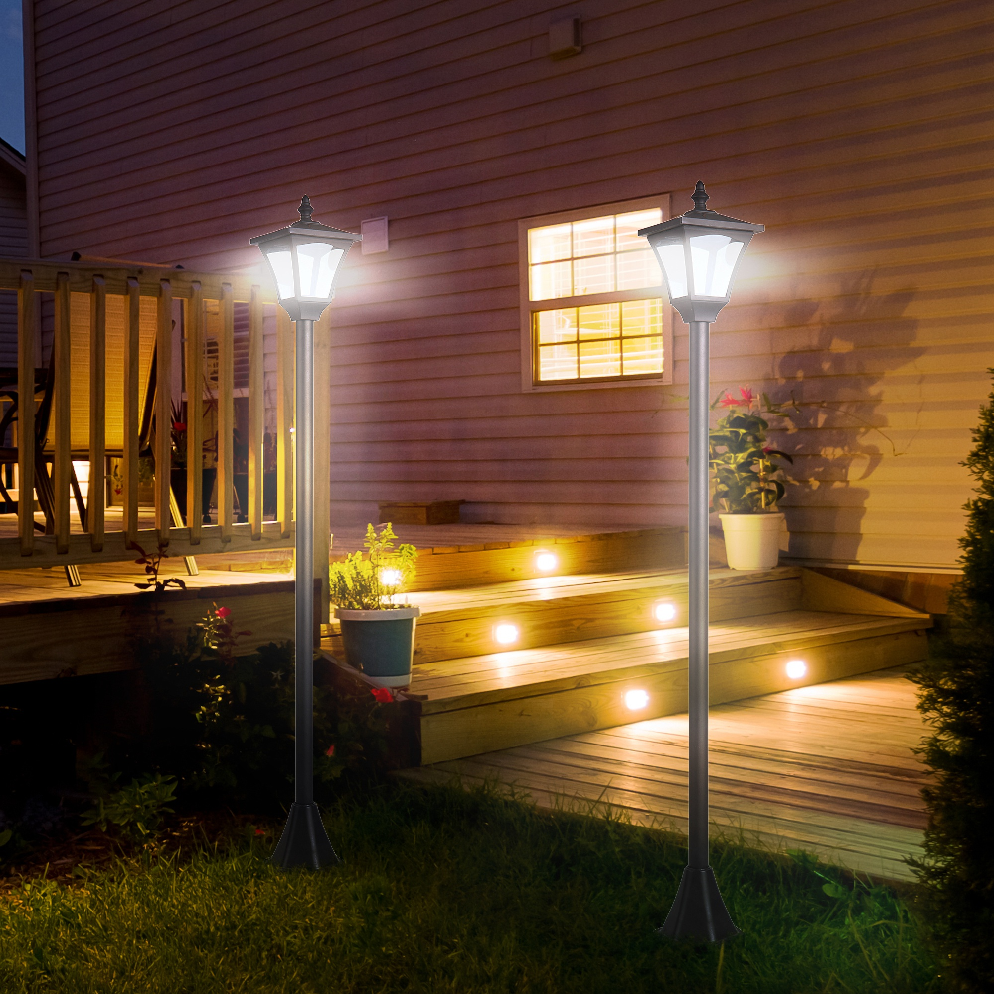 Dos lámparas exteriores iluminan una terraza por la noche, con una casa al fondo.