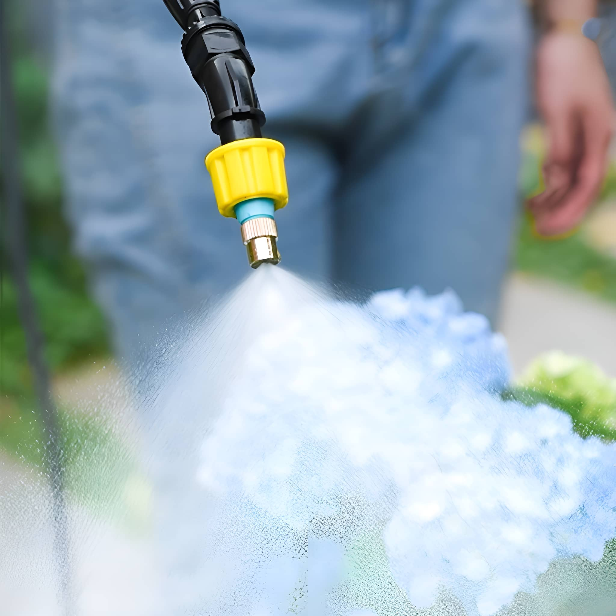 Eine Sprühdüse gibt Wasser auf blaue Blumen ab. Eine Person hält das Sprühgerät.