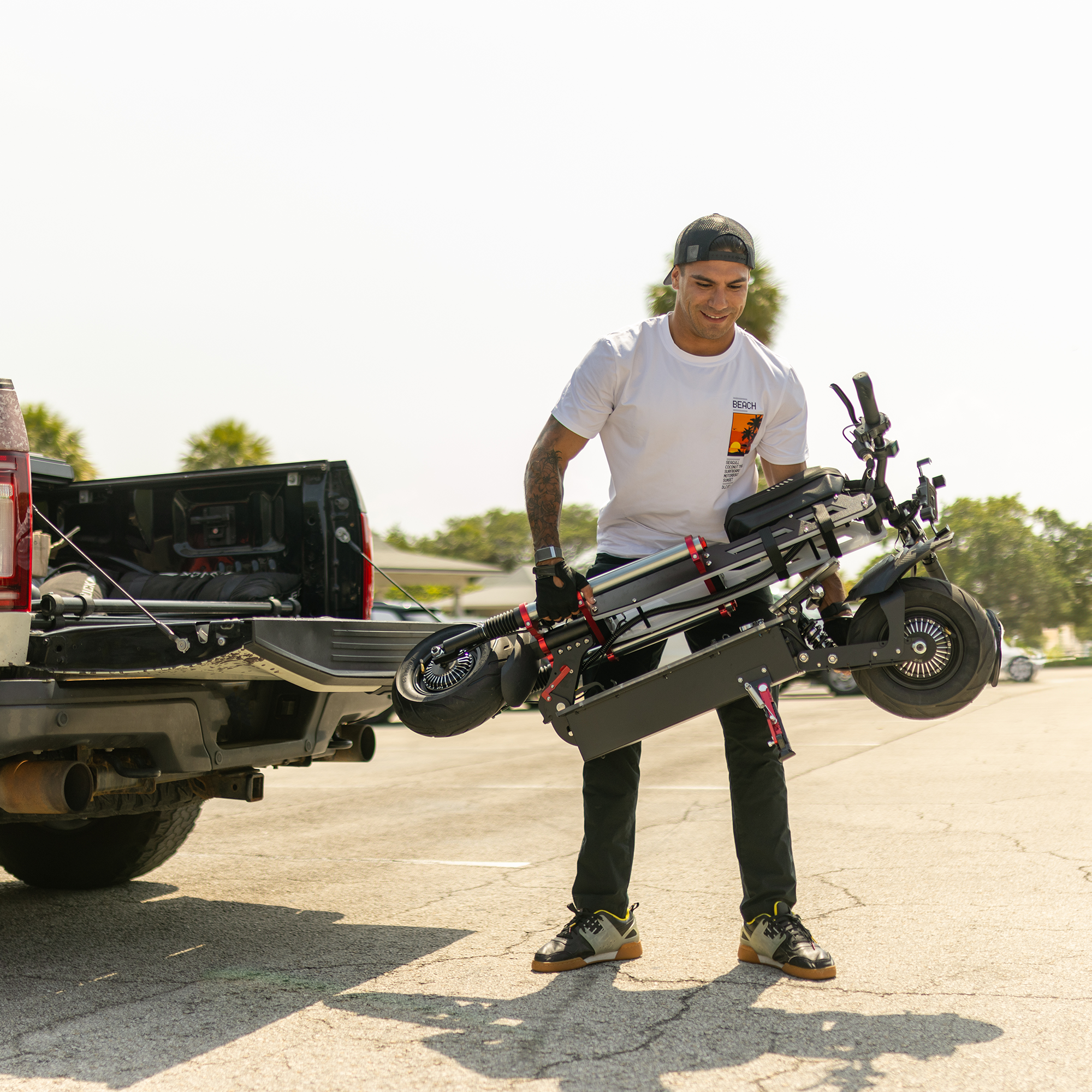 Mężczyzna trzymający złożoną czarną hulajnogę, stojący w pobliżu czarnej ciężarówki.