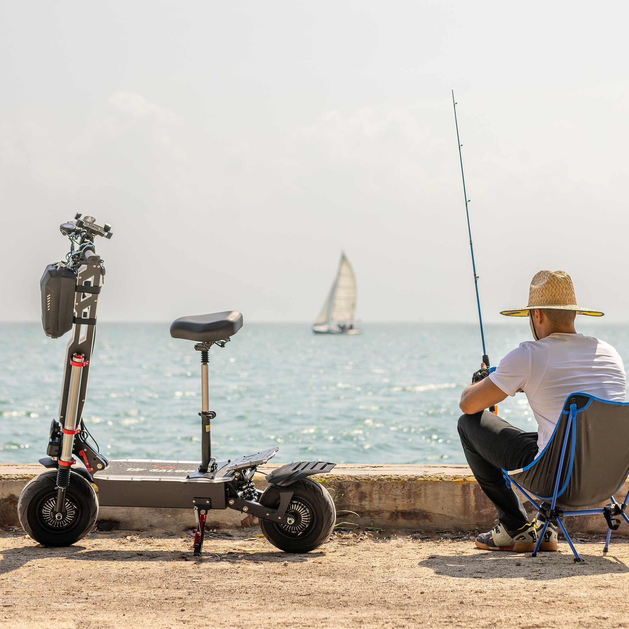 Mężczyzna wędkujący na molo, w pobliżu hulajnoga elektryczna, żaglówka w tle. Słoneczny dzień.