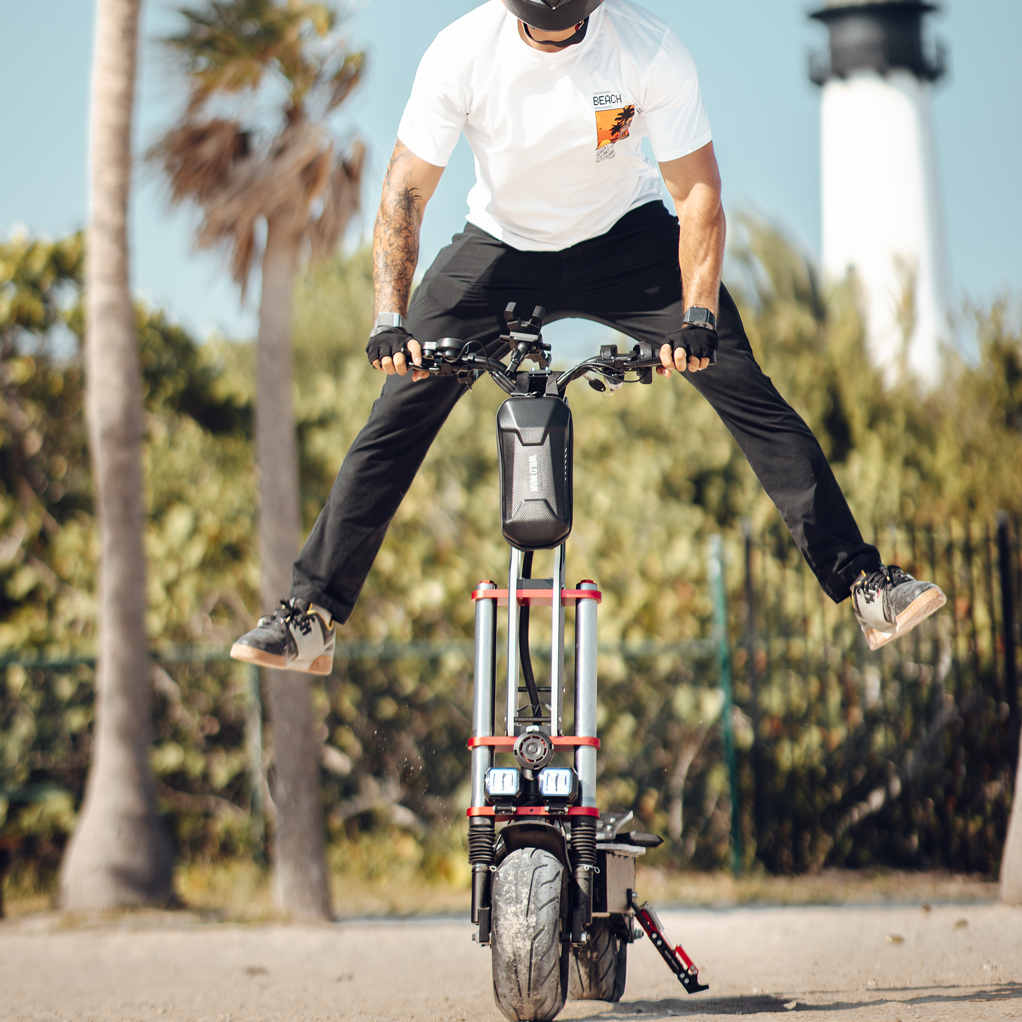 Mężczyzna skaczący na skuterze w parku, w tle palmy i latarnia morska.