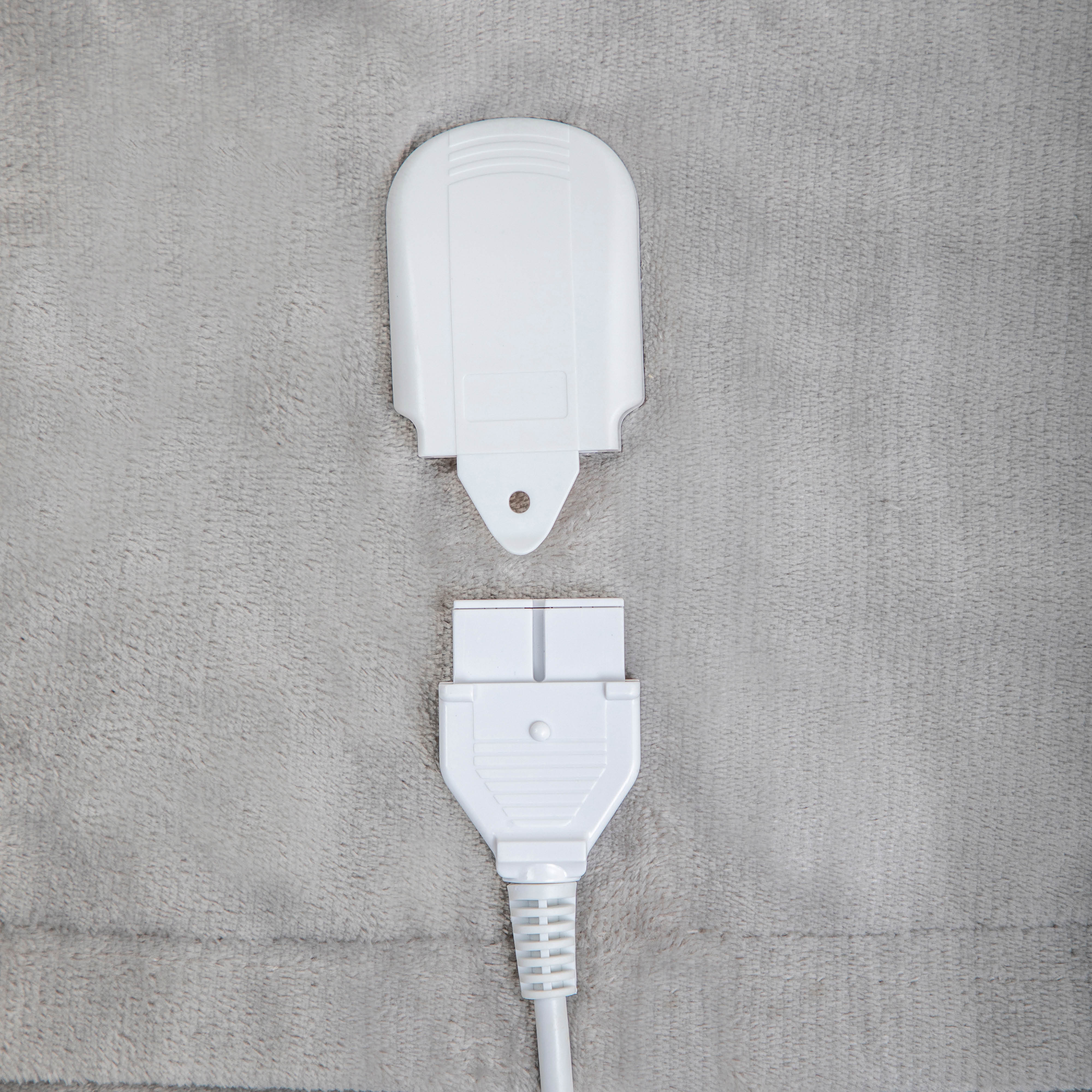 White electric blanket connector and power cord on a gray, fuzzy surface.