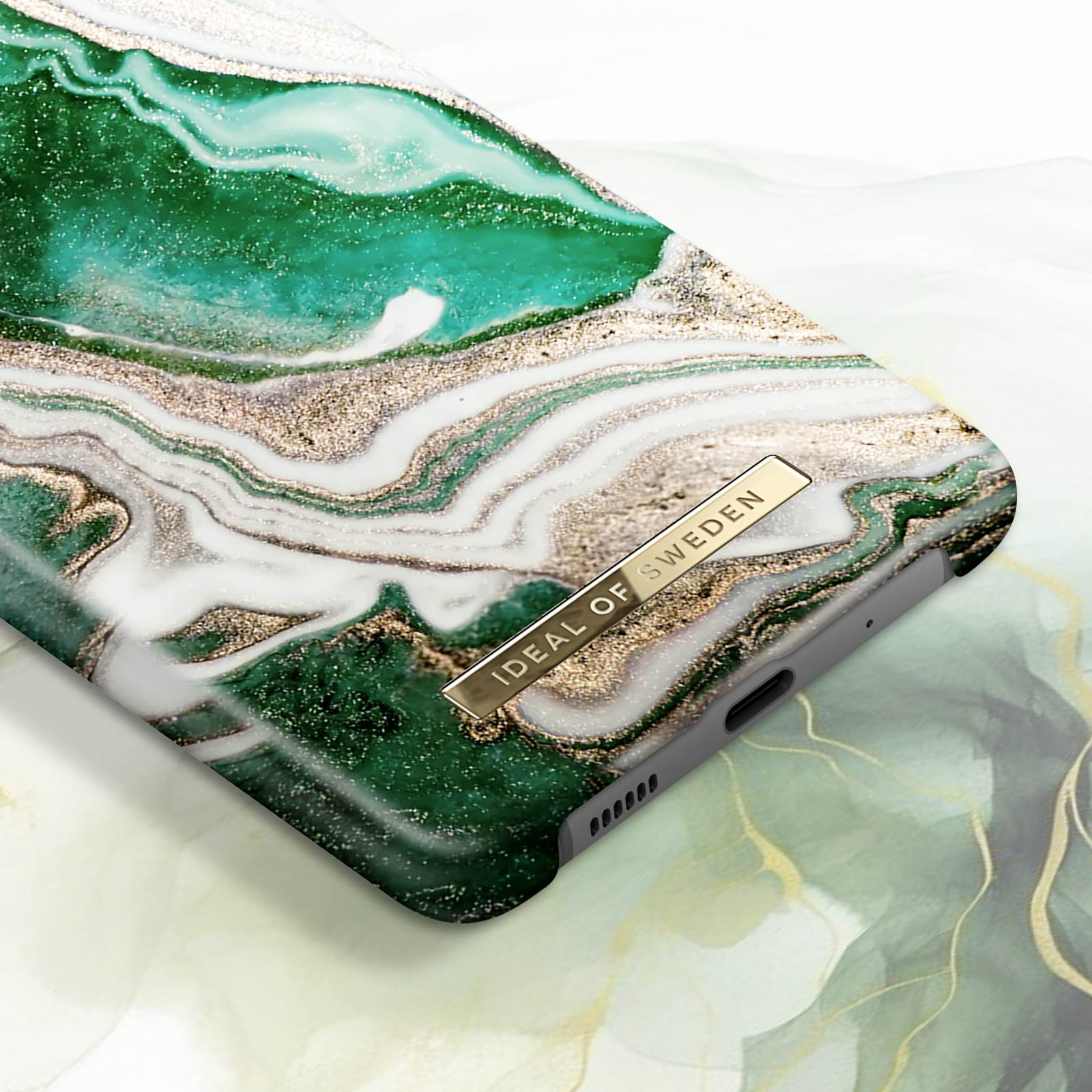 Primo piano di una custodia per telefono con design a marmo verde e bianco, dettagli dorati e logo dorato.