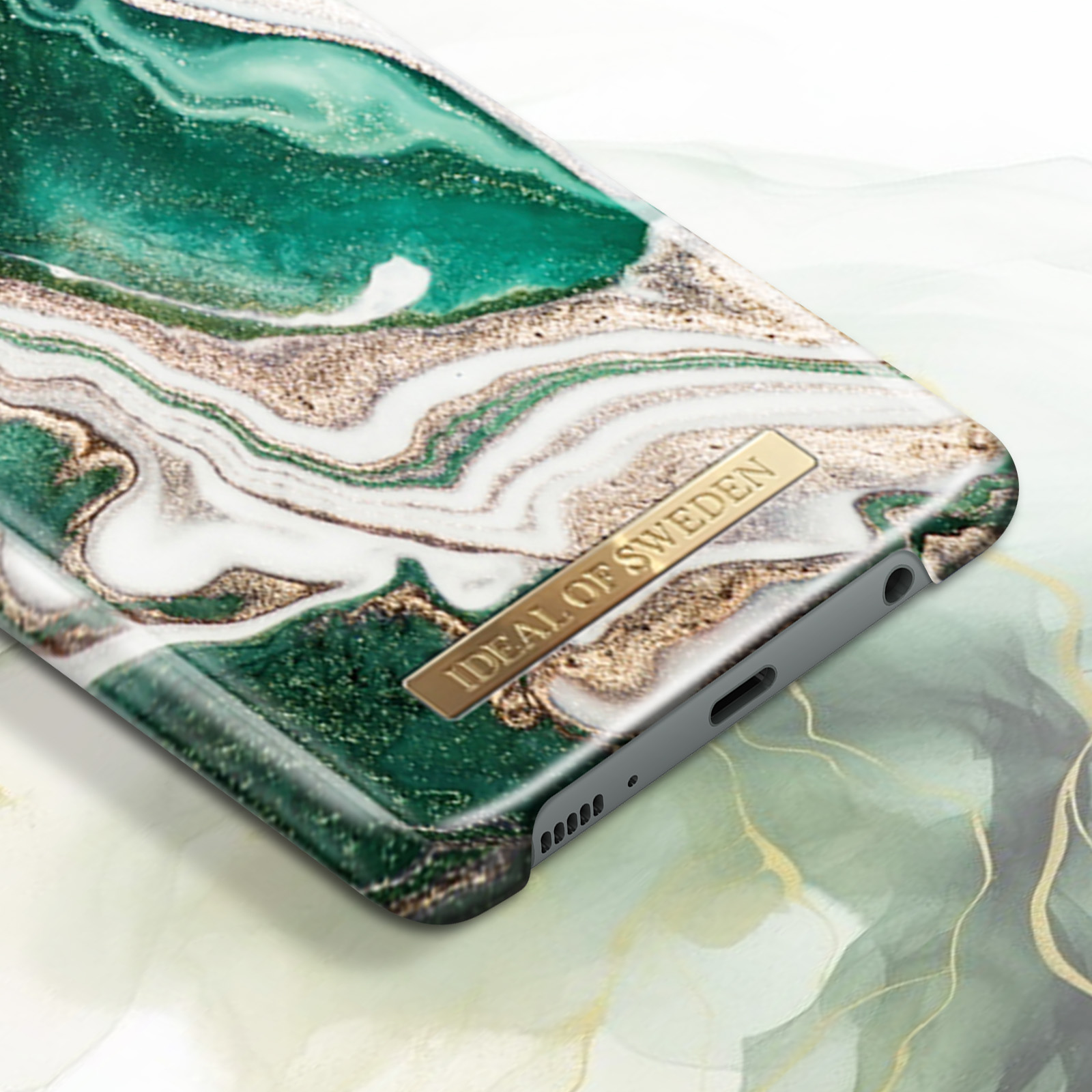Custodia per telefono con design marmorizzato, verde e oro. Il marchio è in basso. Primo piano.