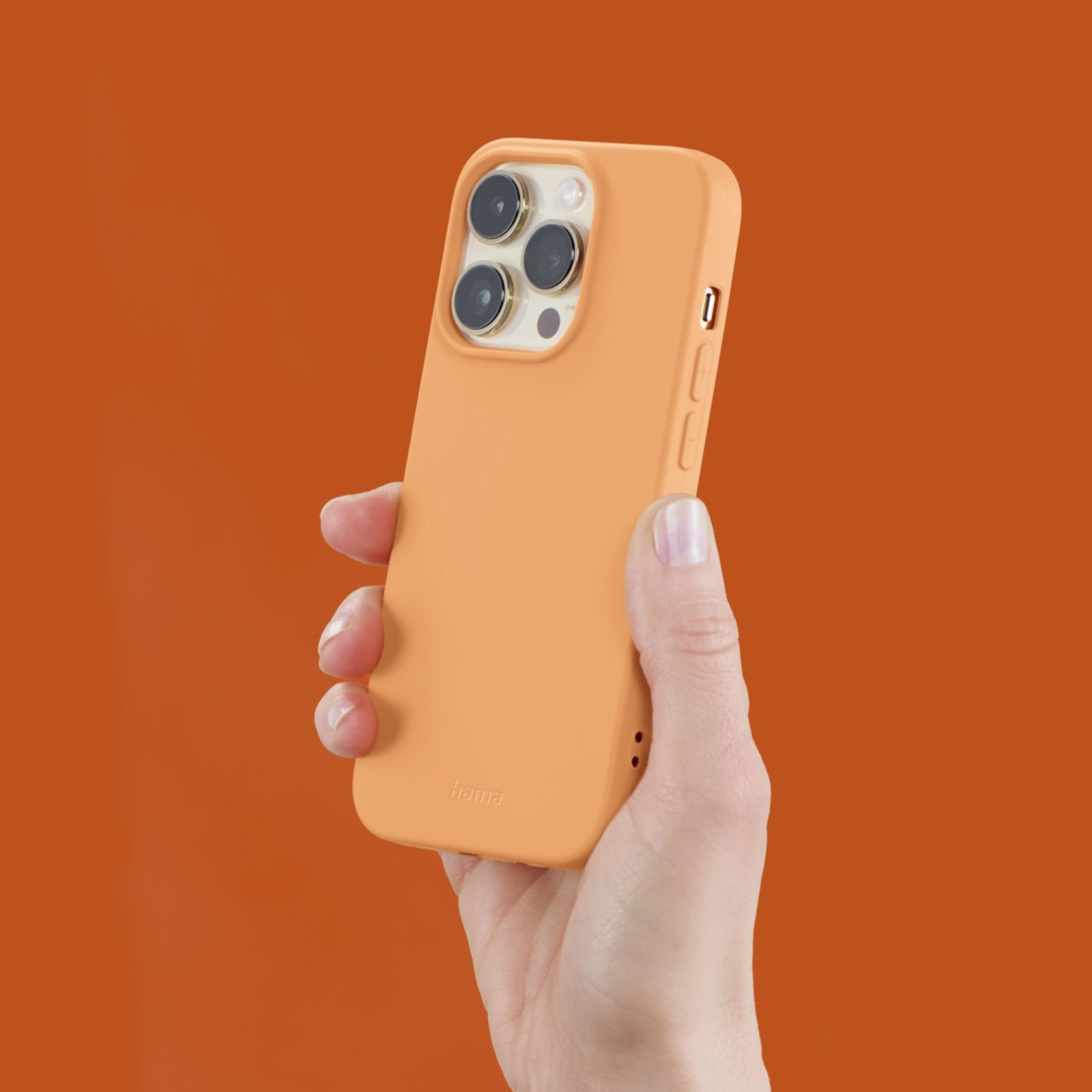 Main tenant une coque de téléphone orange, sur fond orange.