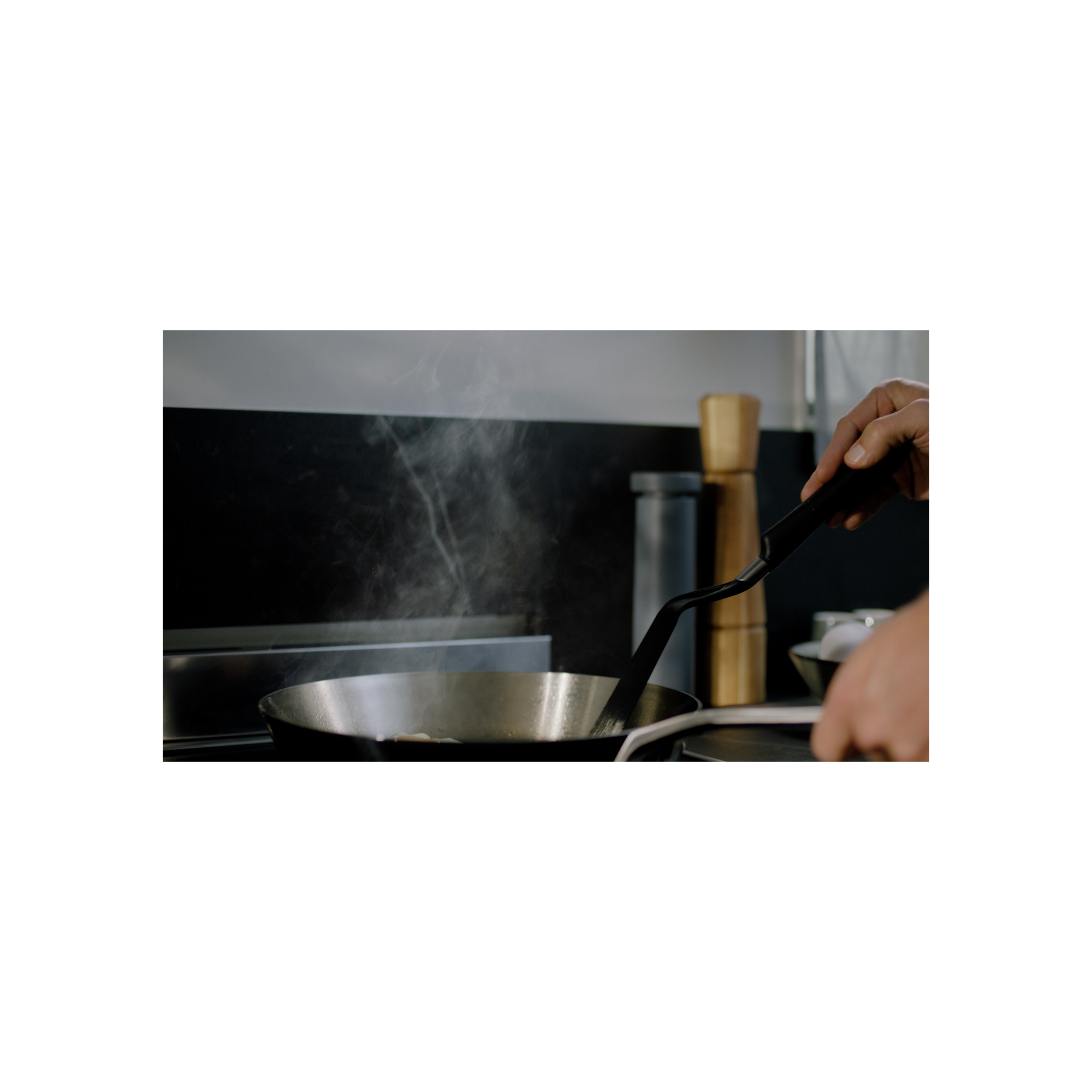 Una persona che cucina in una padella, con vapore che sale. Sfondo scuro, padella nera.
