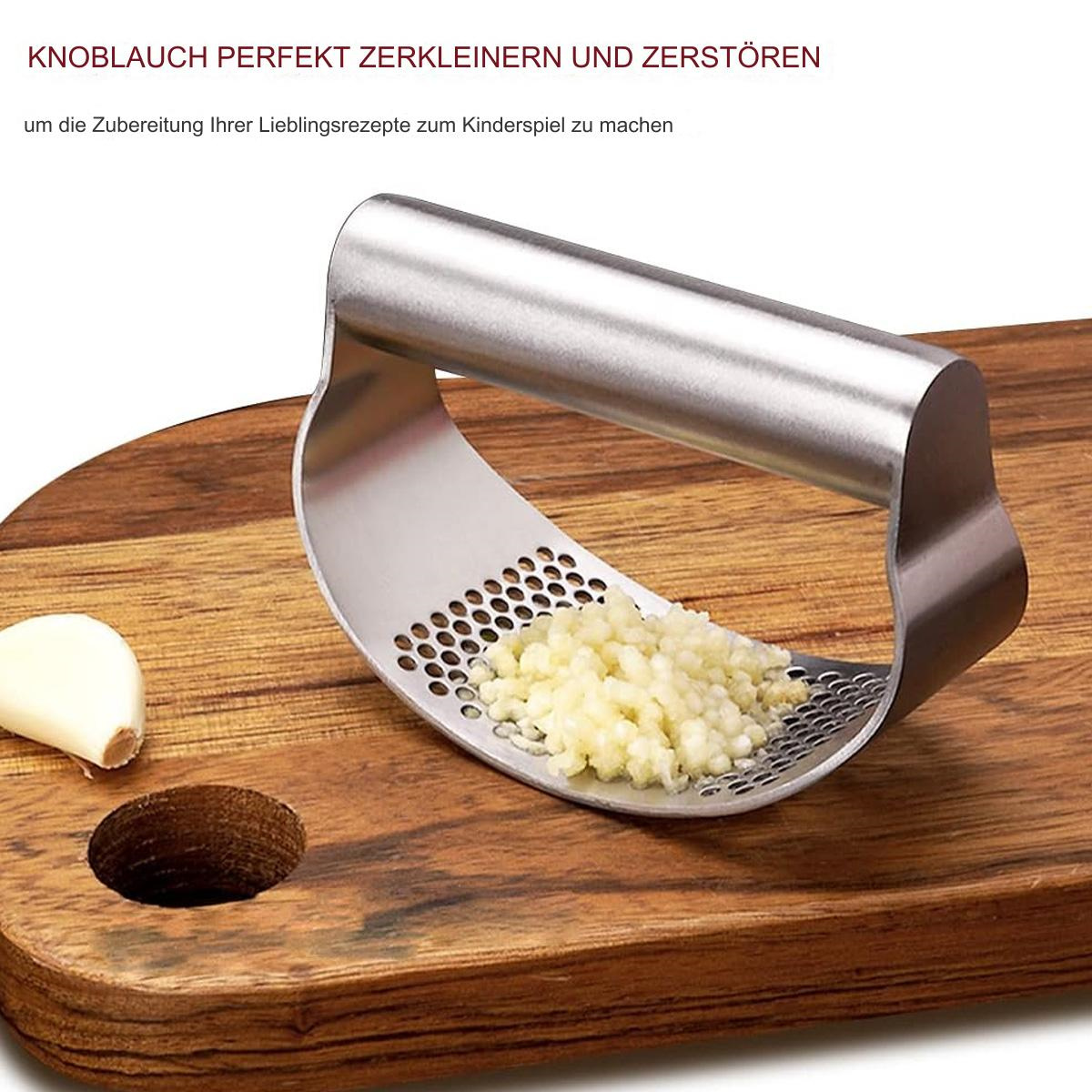 Knoblauchpresse mit gehacktem Knoblauch auf einem Holzschneidebrett mit einer Knoblauchzehe.