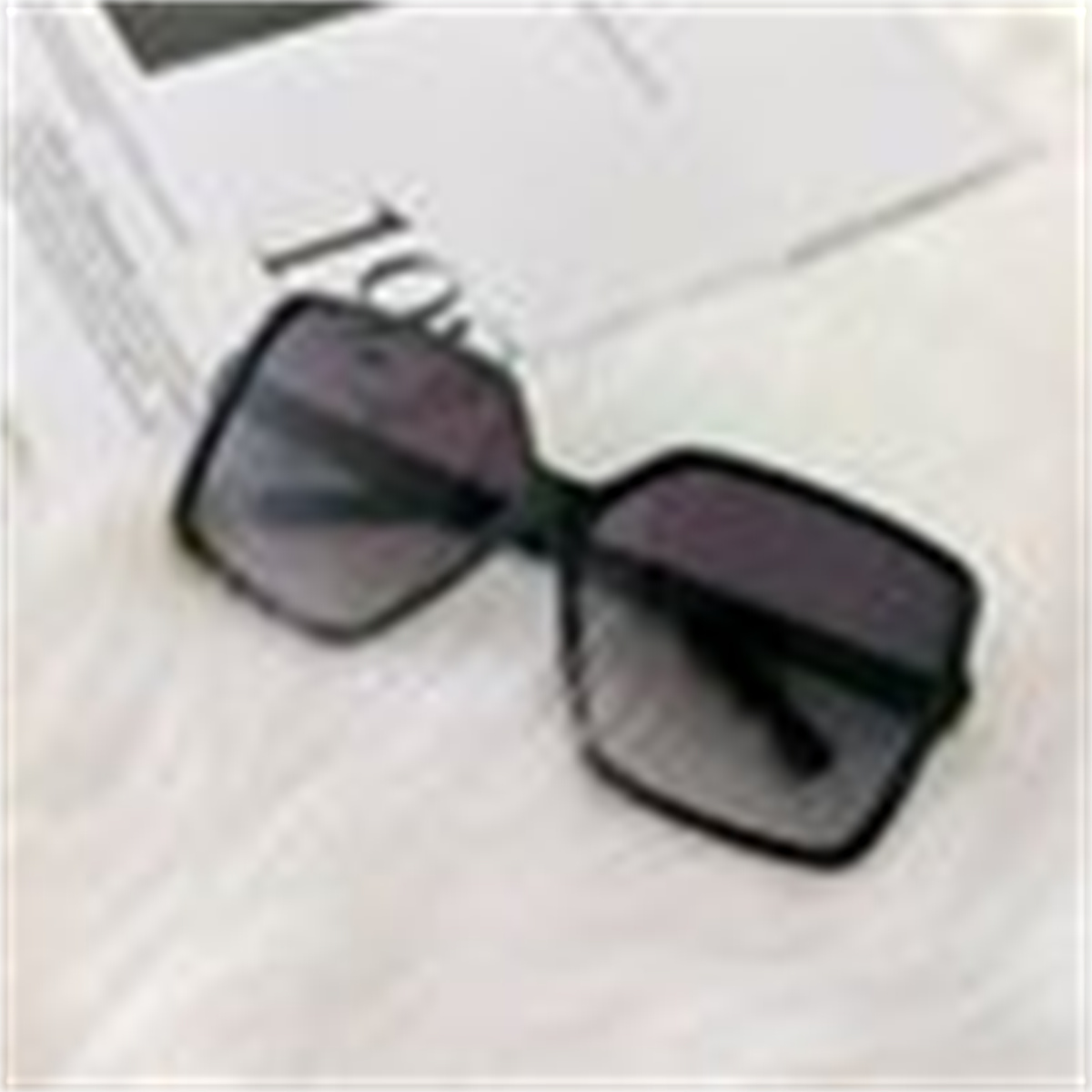 Schwarze Sonnenbrille mit dunklem Farbverlauf auf einer weißen, flauschigen Oberfläche.