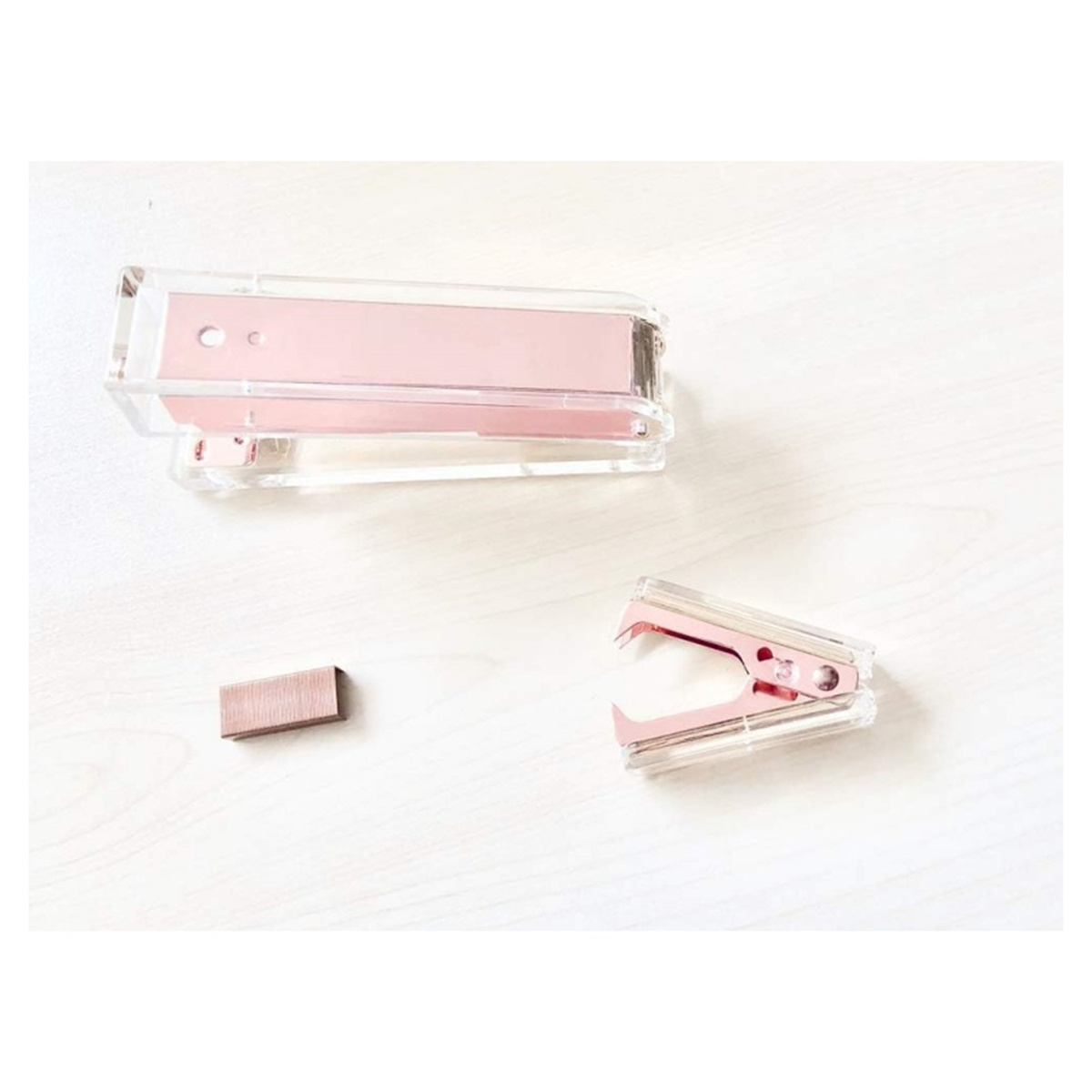Rosa und transparentes Hefter- und Entferner-Set und Heftklammern auf weißer Oberfläche. Draufsicht.