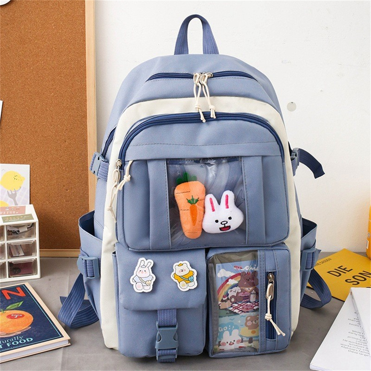 Blauer und weißer Rucksack mit einer transparenten Vordertasche mit einer Karotte und einem Hasen. Andere Taschen und Aufkleber sichtbar.