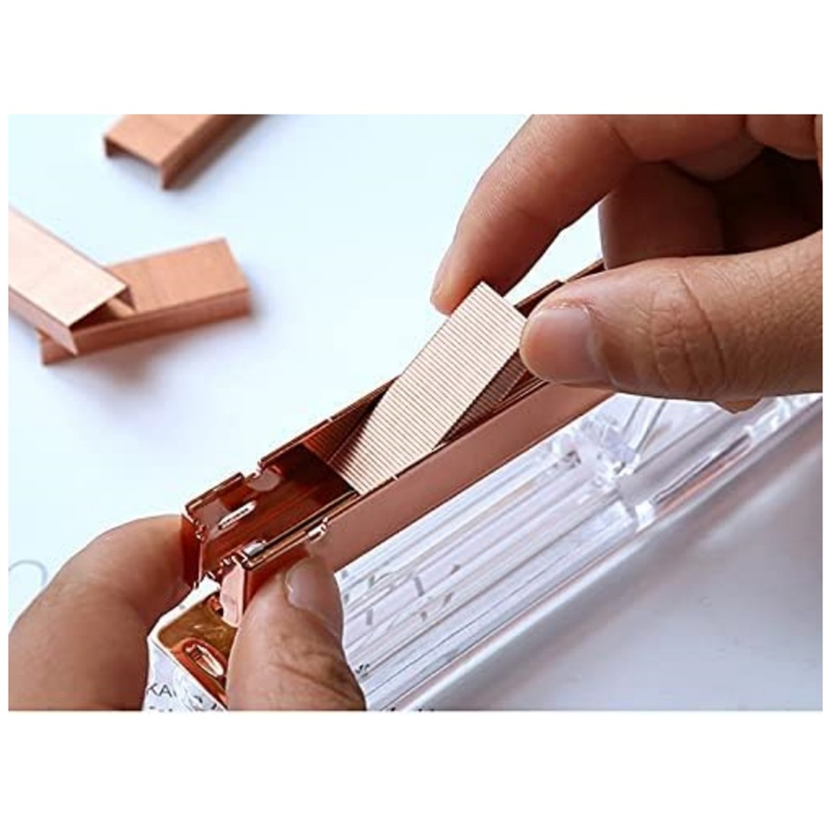 Hand legt Heftklammern in einen Tacker. Heftklammern kupferfarben, Tacker transparent.