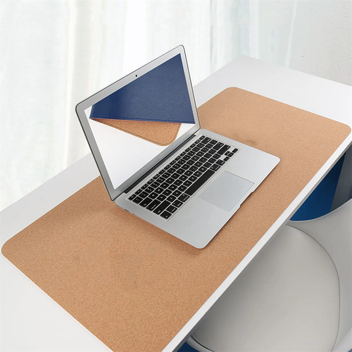 Laptop auf einem Schreibtisch mit einer Korkmatte. Ein blaues und braunes Pad ist hinter dem Laptop-Bildschirm platziert.