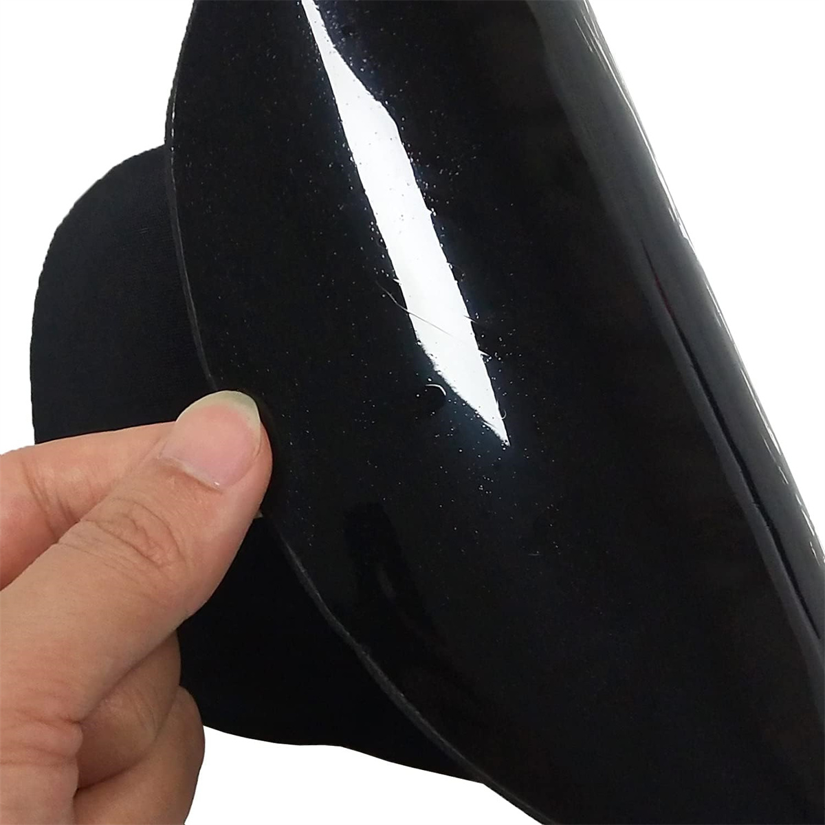 Hand hält ein schwarzes, glänzendes Material und gibt eine darunterliegende Schicht frei.
