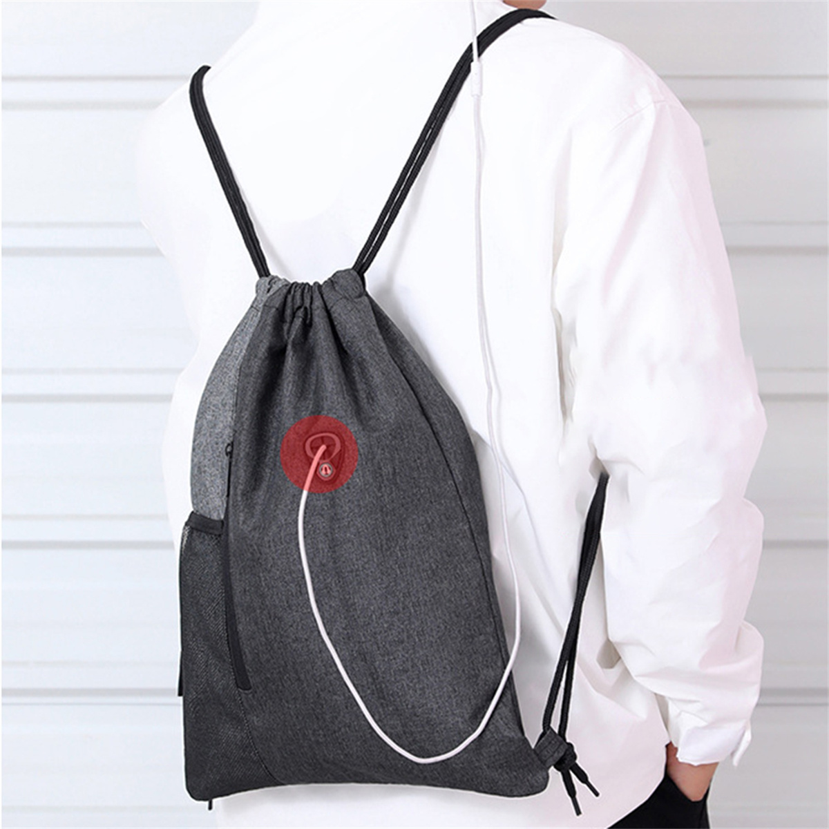 Person mit grauem Rucksack mit Kordelzug, schwarzen Schnüren und einem weißen Kabel mit rotem Kreis.