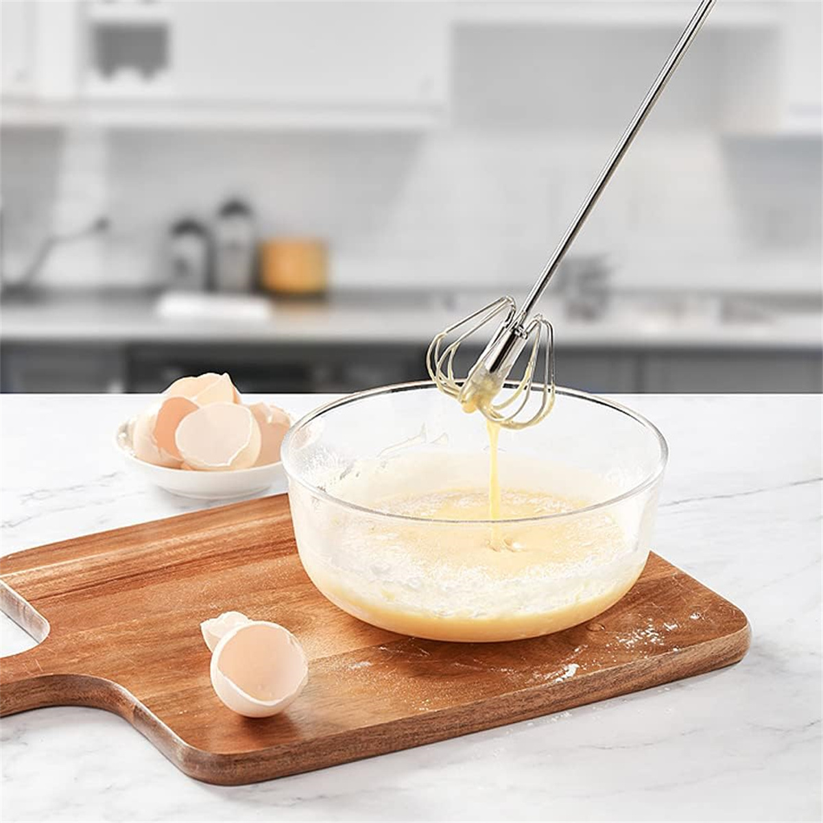 Eier werden in einer Glasschüssel auf einem Holzschneidebrett verquirlt. Eierschalen liegen auf einem Teller.