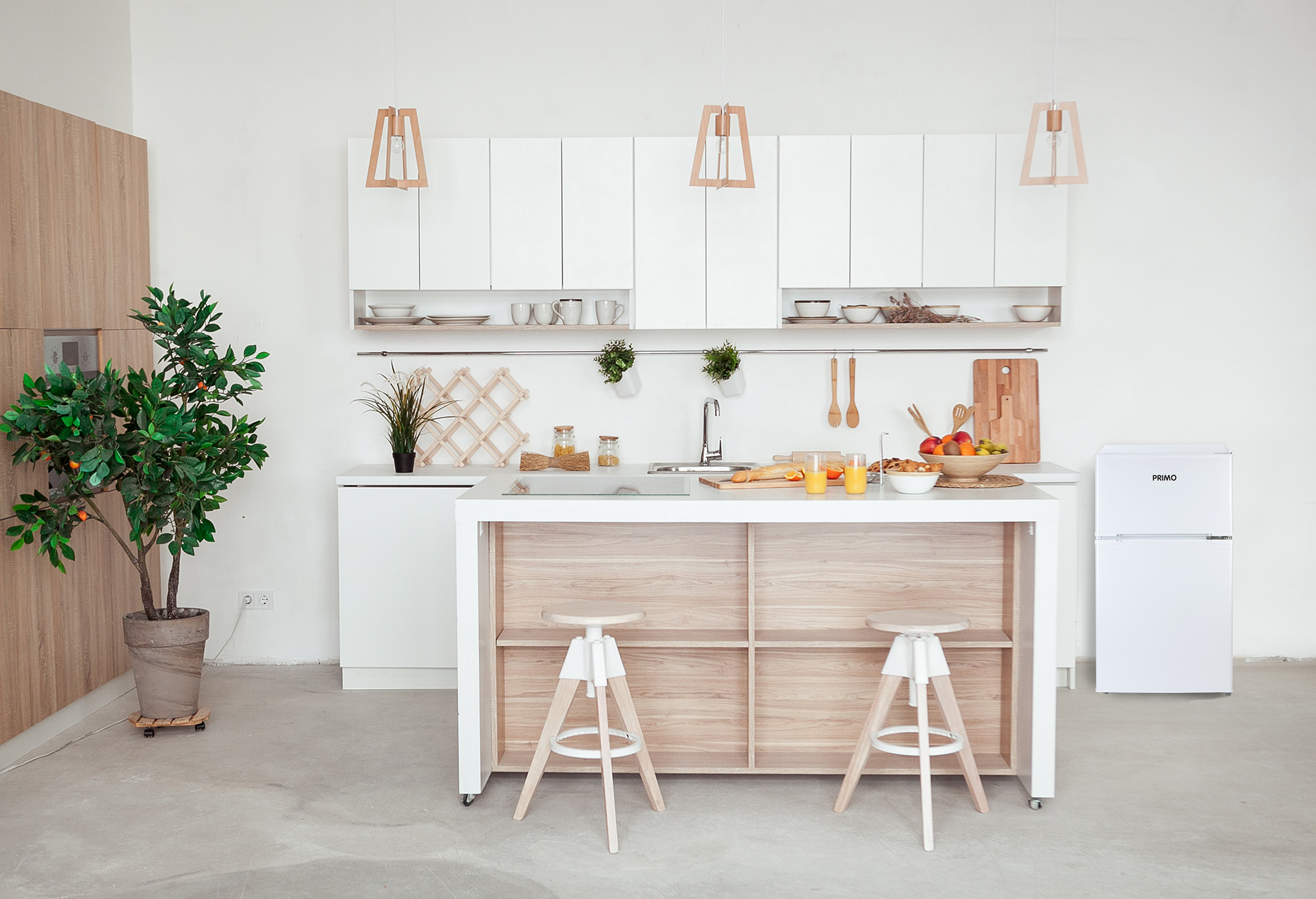 Cuisine moderne avec des armoires blanches, un îlot en bois avec des tabourets et un réfrigérateur blanc. Une plante et des fruits sont visibles.