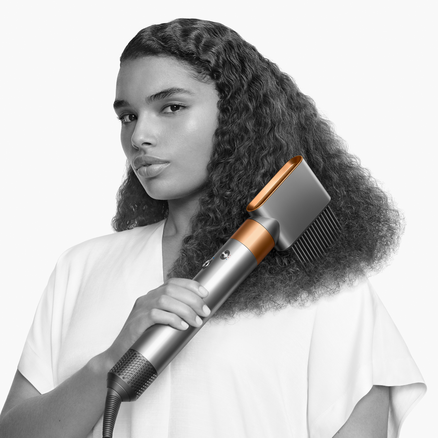 Donna con capelli ricci che usa lo strumento Dyson. Dispositivo color argento e rame.