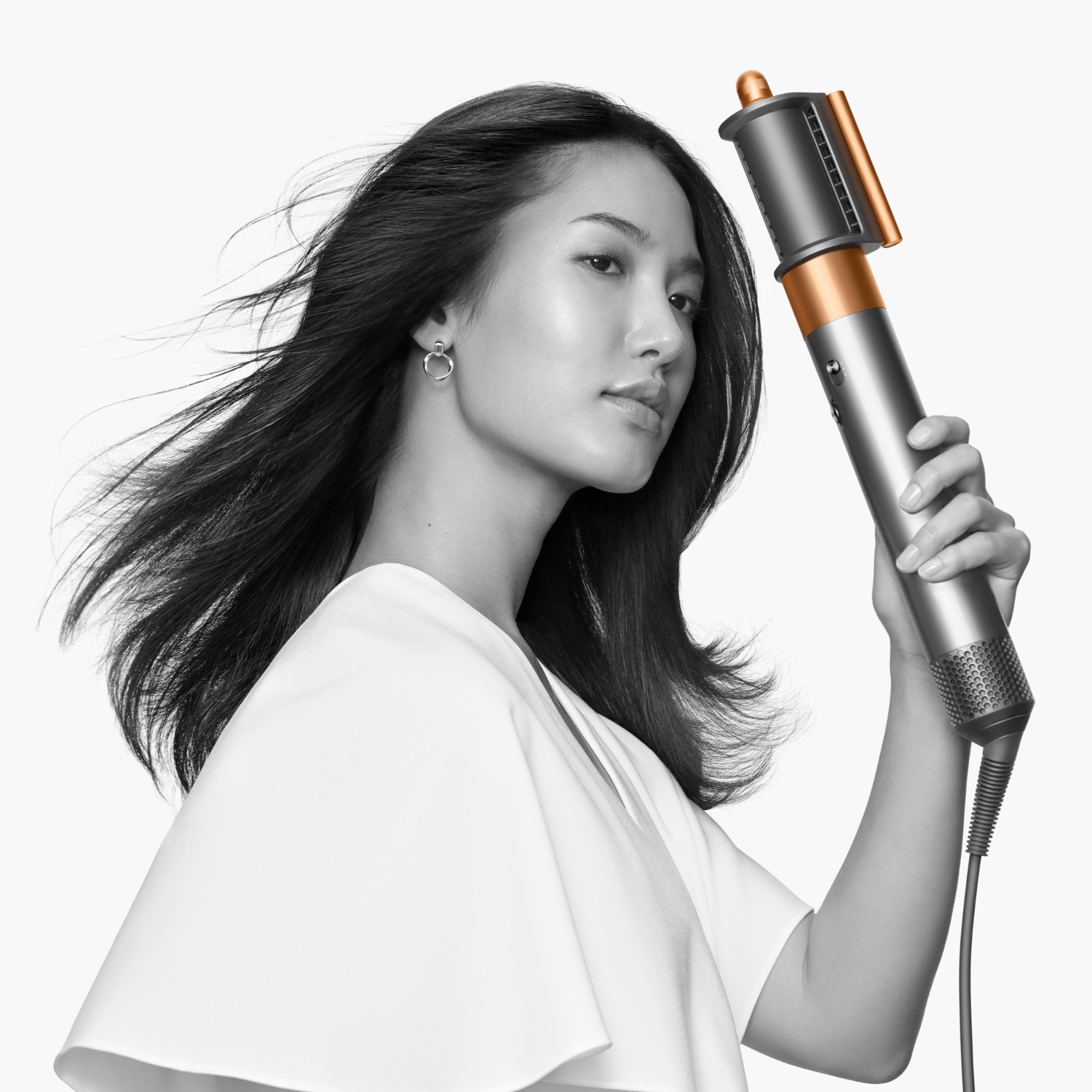 Donna con lunghi capelli scuri che usa lo strumento Dyson. Dispositivo color argento e rame.