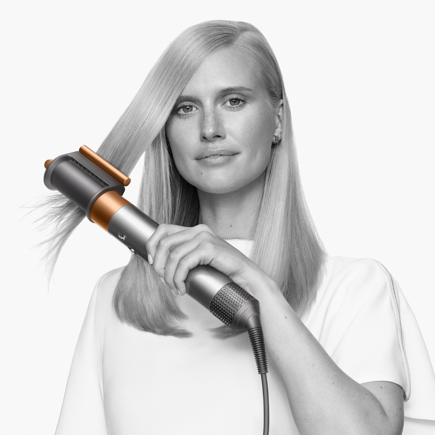 Donna con capelli biondi che usa lo strumento Dyson. Dispositivo color argento e rame.