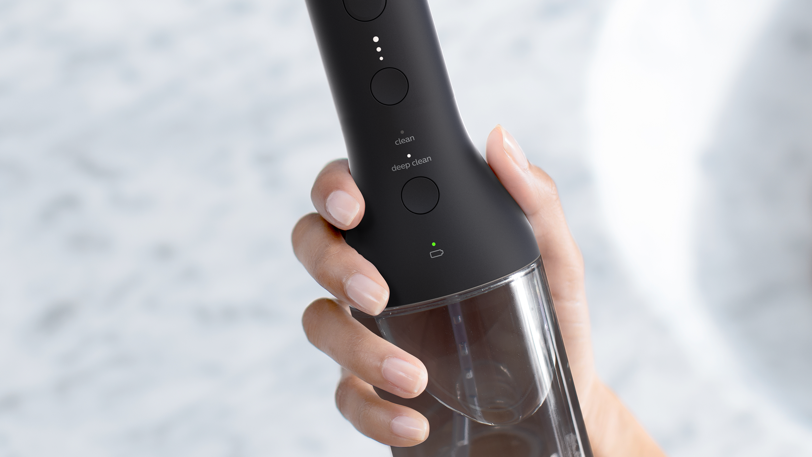 Eine Hand hält ein schwarzes Gerät mit Knöpfen und einem transparenten Wasserbehälter. Der Hintergrund ist unscharf.