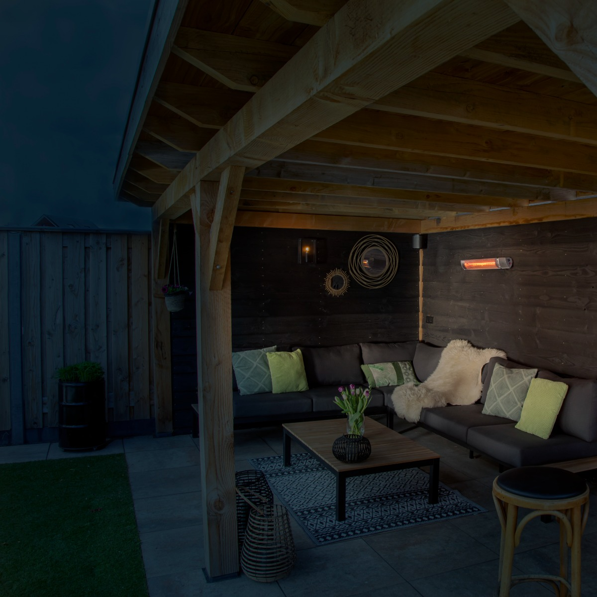 Buitenlounge onder een houten pergola met een donkergrijze bank, kussens en een zwarte tafel.