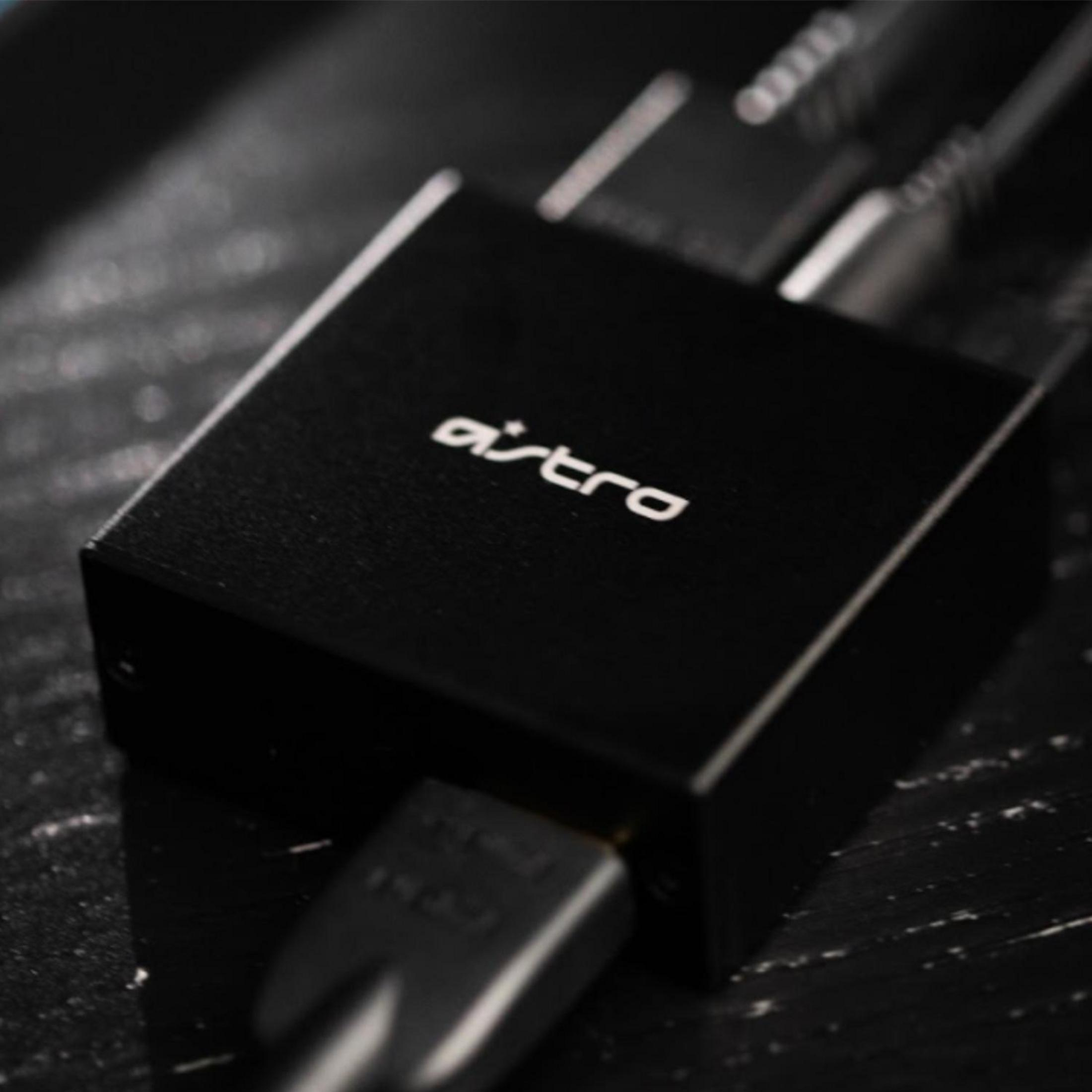 Czarny adapter audio Astro z podłączonymi kablami, na ciemnej drewnianej powierzchni, zbliżenie.