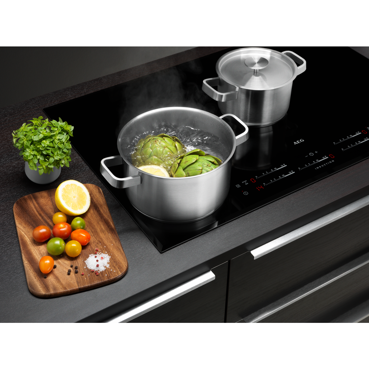 Escena de cocina: alcachofas hirviendo, limones, tomates, ollas y una planta.