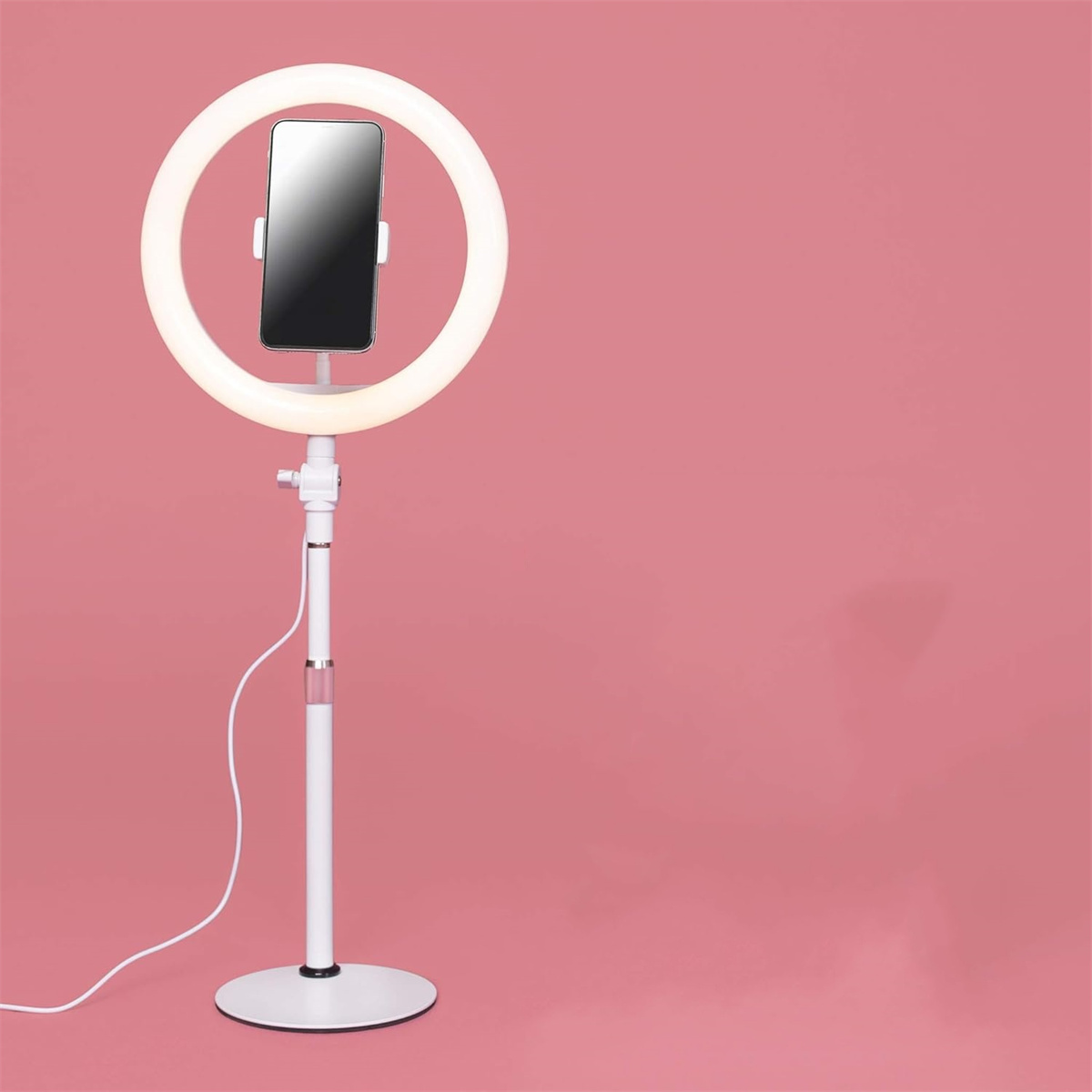 Ringlicht mit Telefonhalter auf Ständer, rosa Hintergrund.