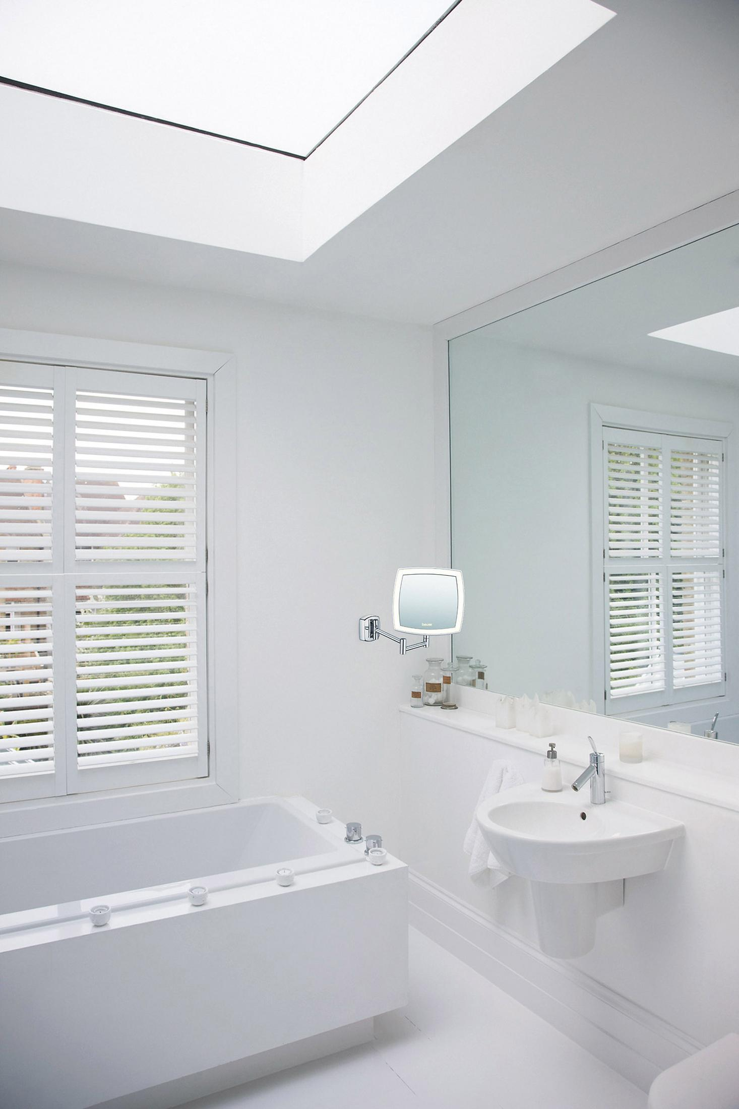 Bagno bianco con specchio, lavandino e finestra con persiane. Vasca da bagno bianca visibile.