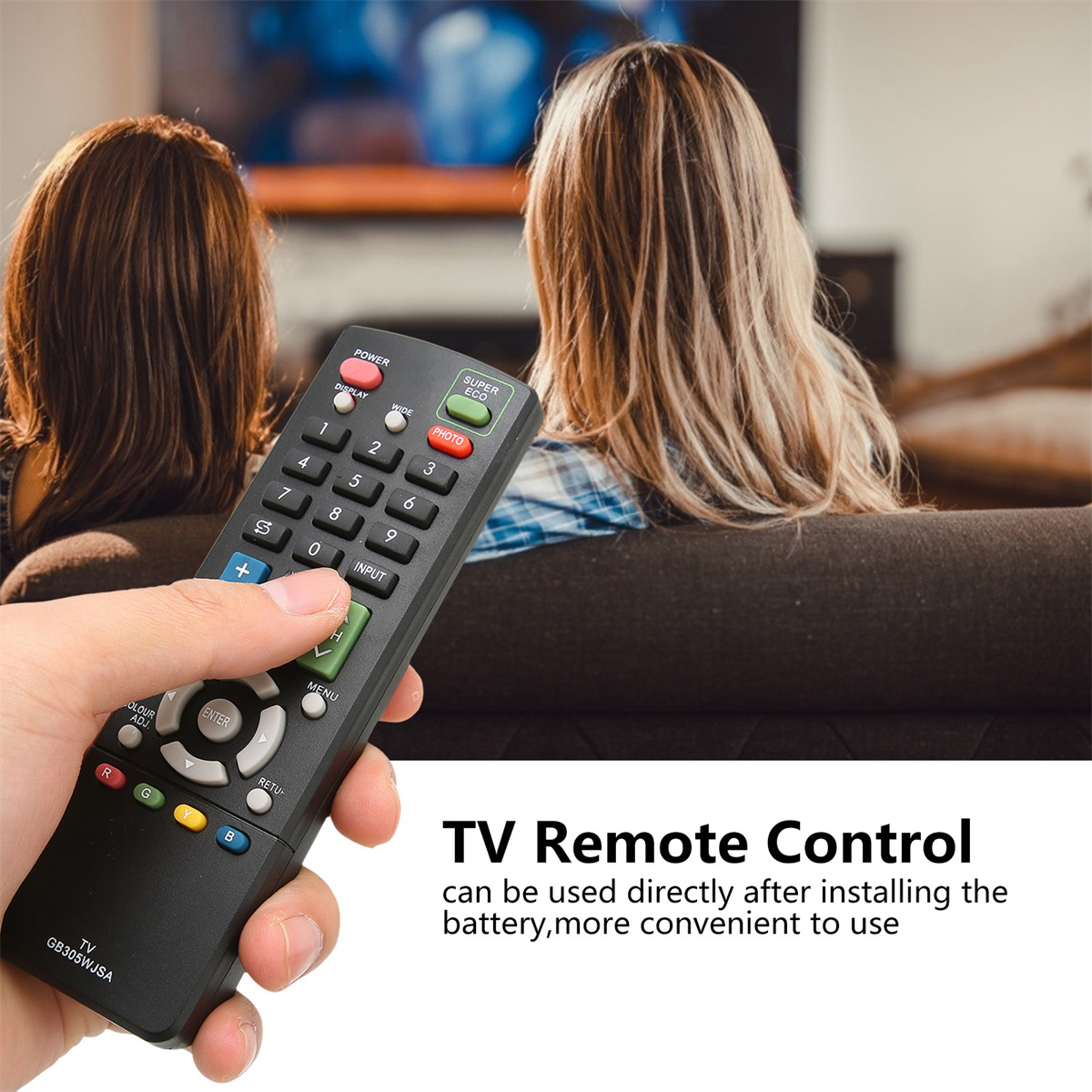 Eine Hand, die eine TV-Fernbedienung hält. Zwei Personen sitzen im Hintergrund auf einem Sofa.