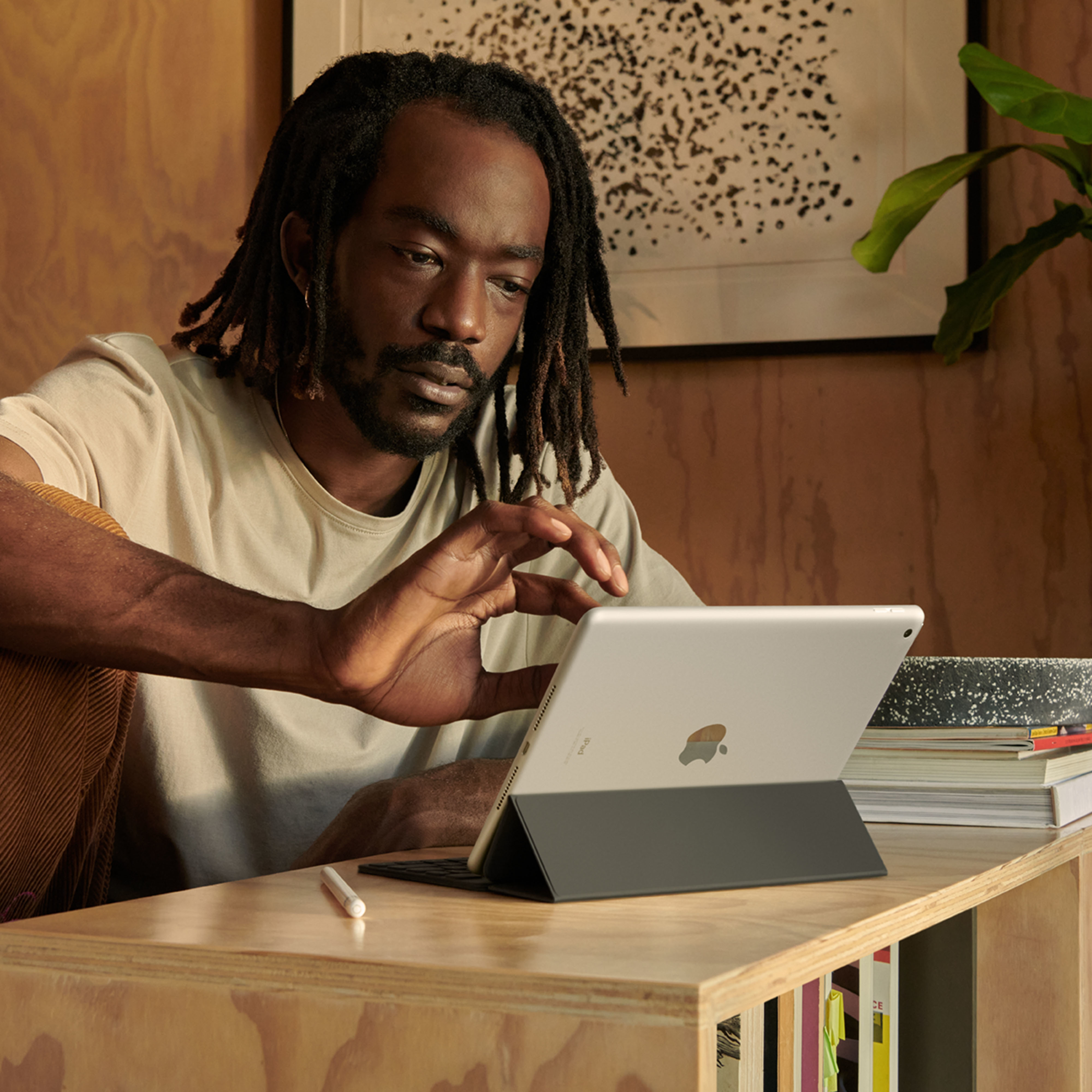 Een man met dreadlocks die een iPad gebruikt, zittend aan een houten bureau met een potlood erop.