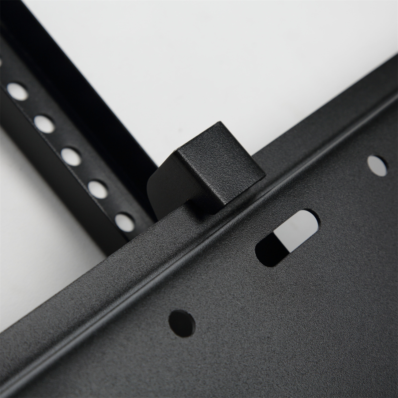 Eine schwarze Metallhalterung mit Löchern und einem gebogenen Teil, montiert auf einer weißen Oberfläche.